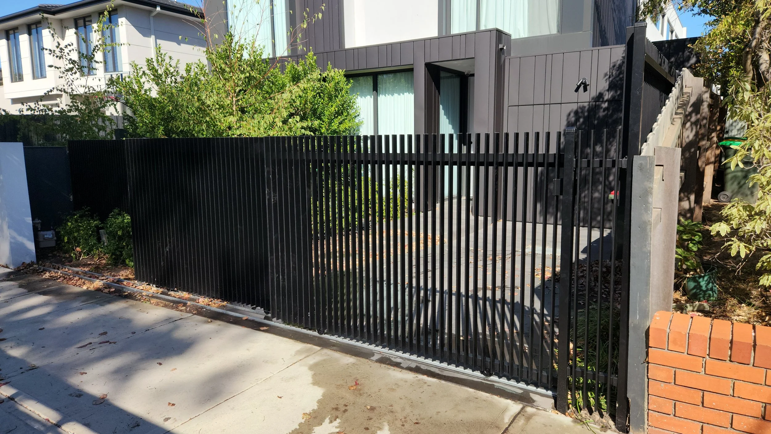 Modern black metal gate with greenery and a contemporary building in the background.