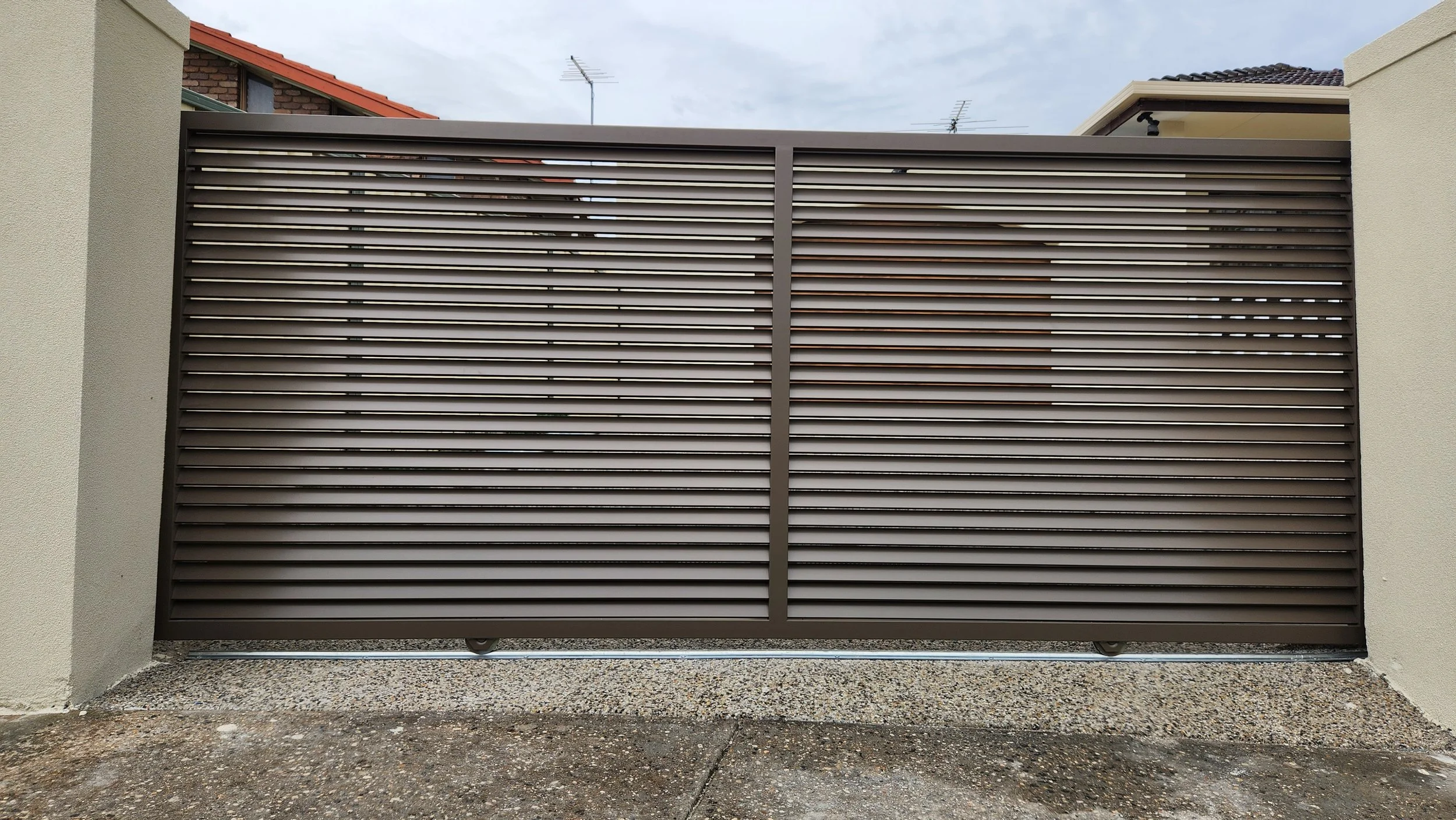 Metal sliding gate with horizontal slats in front of a residential property