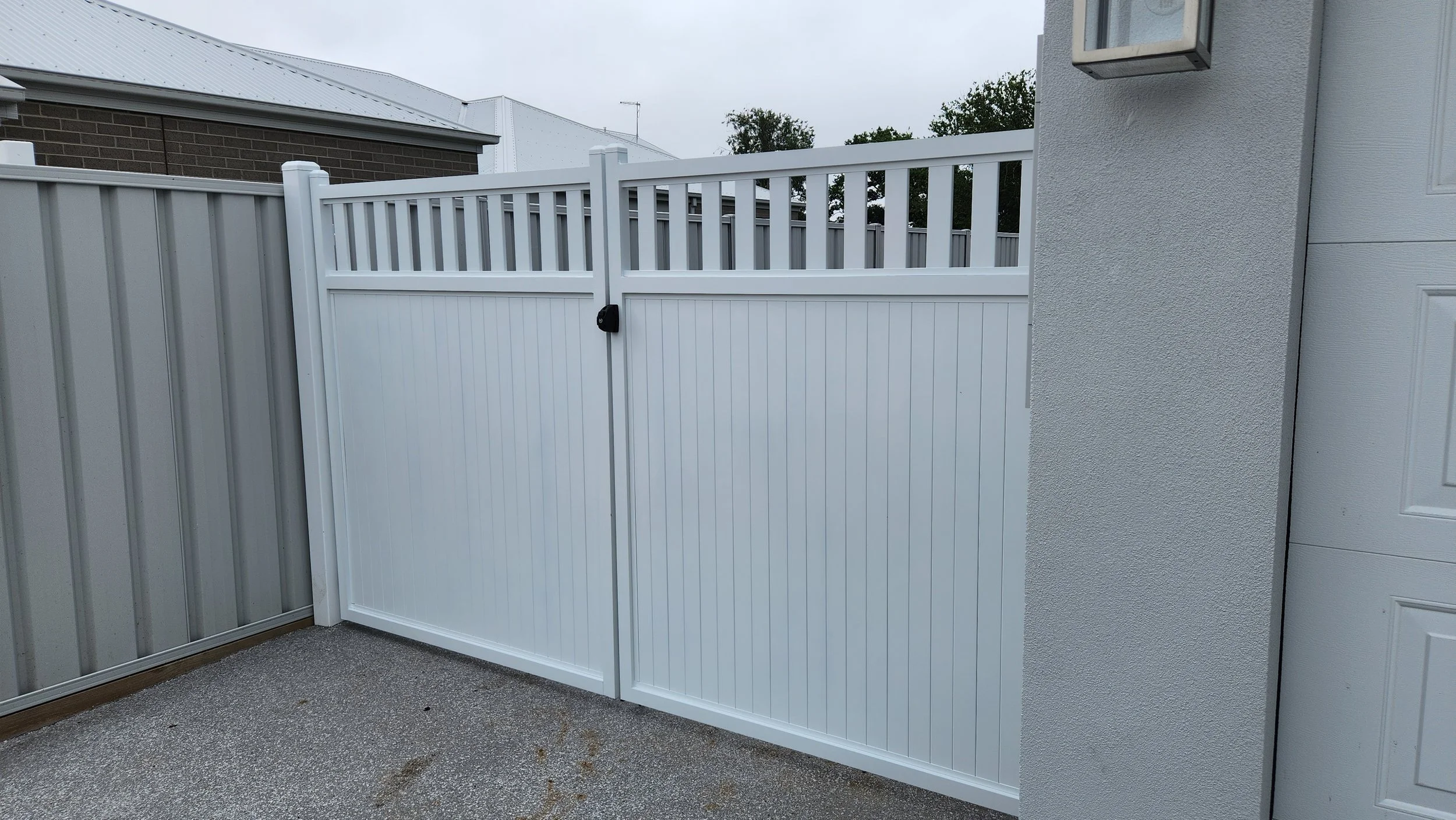 White vinyl fence gate with lock next to a white textured wall.