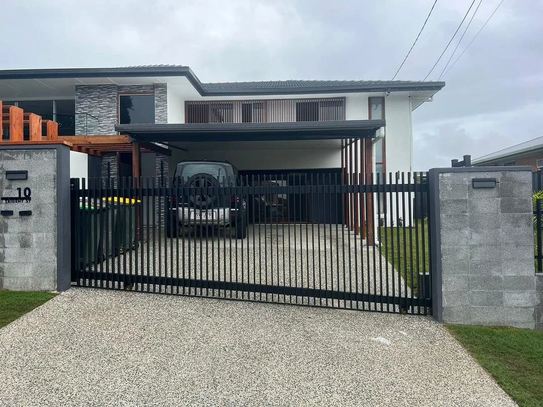 Modern two-story house with a carport, black gate, parked black SUV, two green garbage bins, and a well-maintained front yard with grass.