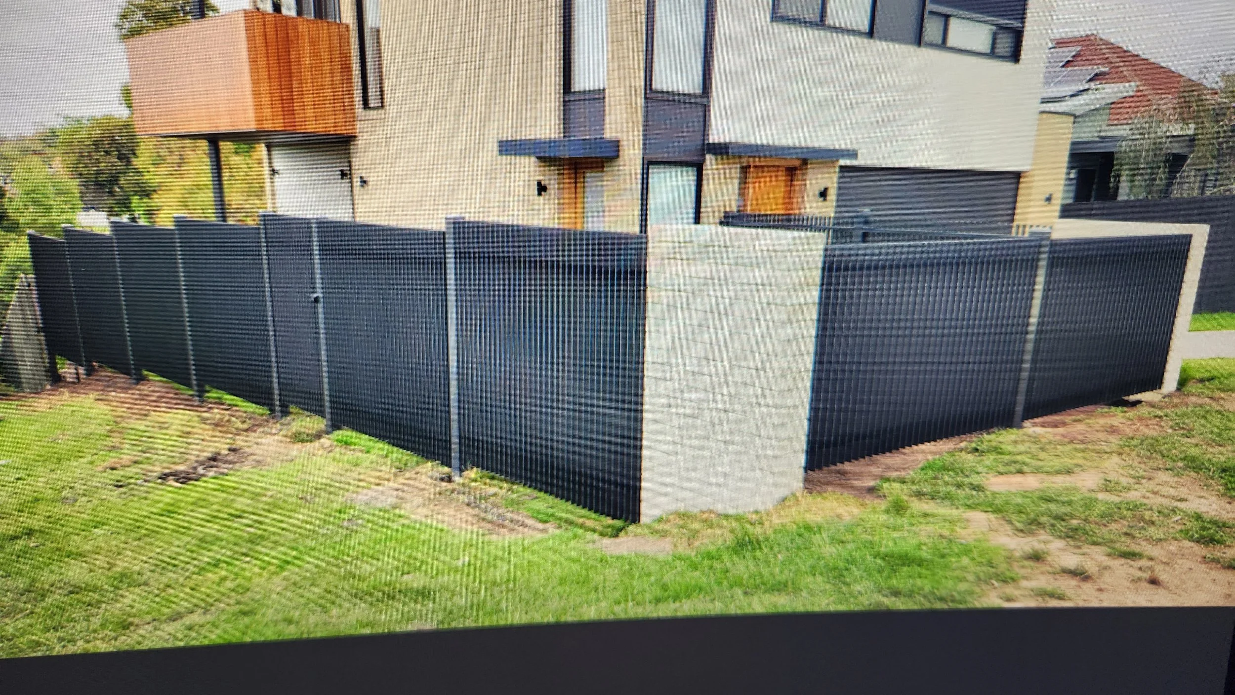 Modern residential house with a black metal fence and a light brick pillar, featuring wooden accents and large windows.