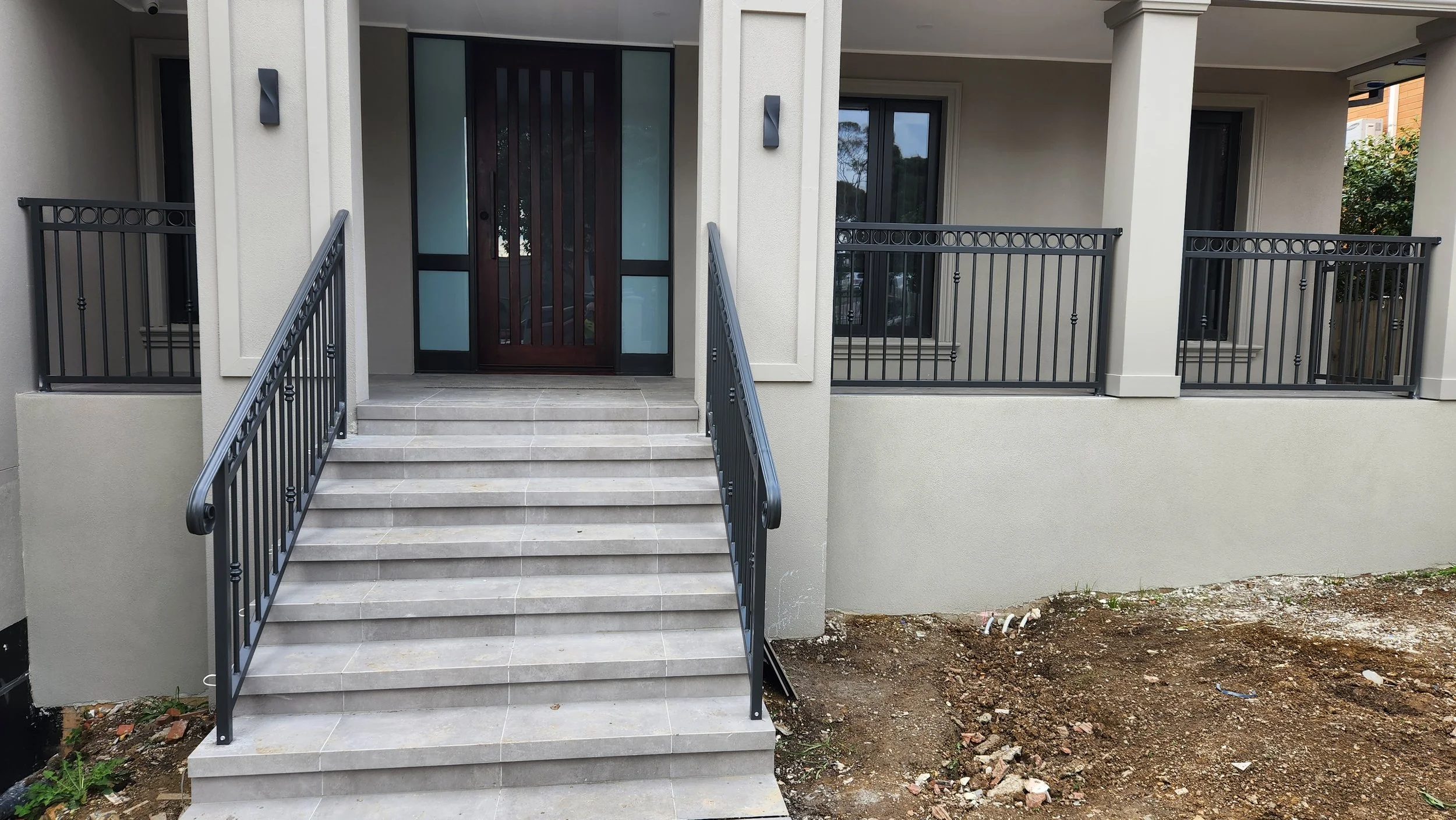 Front entrance with stairs, black railings, glass and wood door, and a beige exterior wall under construction