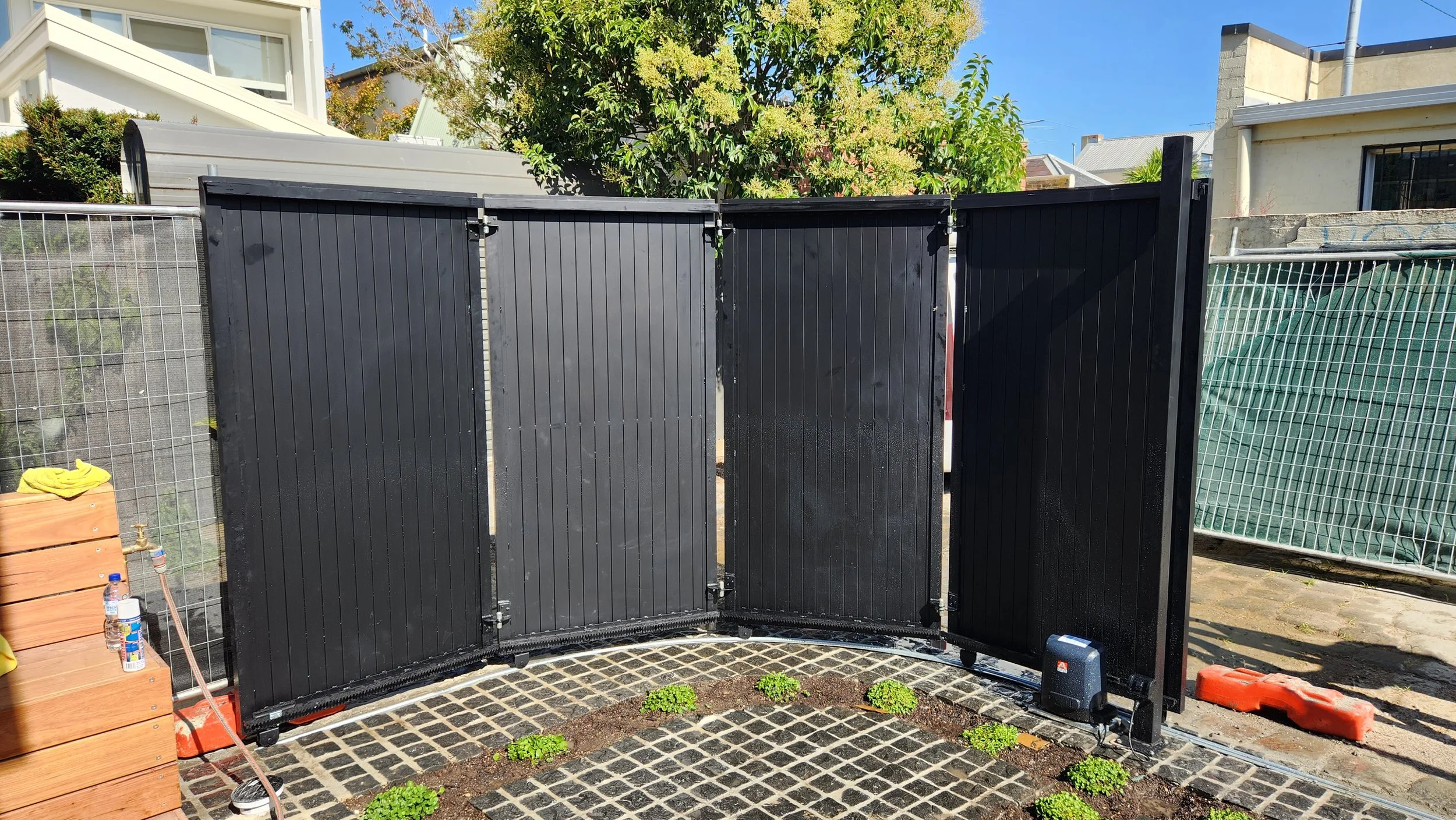Black foldable outdoor privacy screen in a garden, with small green plants in the soil in front.