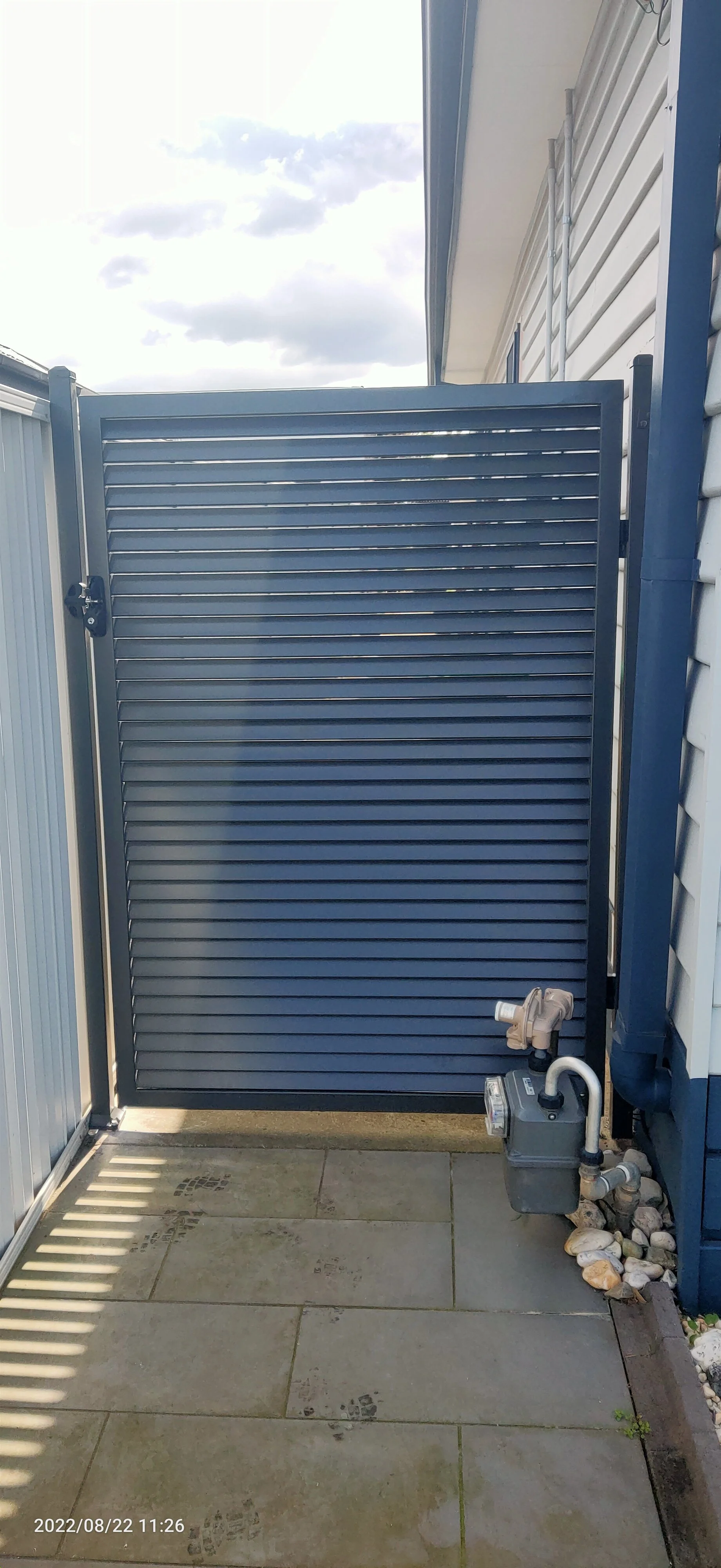 Image of a blue privacy gate with a lock, situated on a patio with stamped concrete floor and decorative rocks on the side.