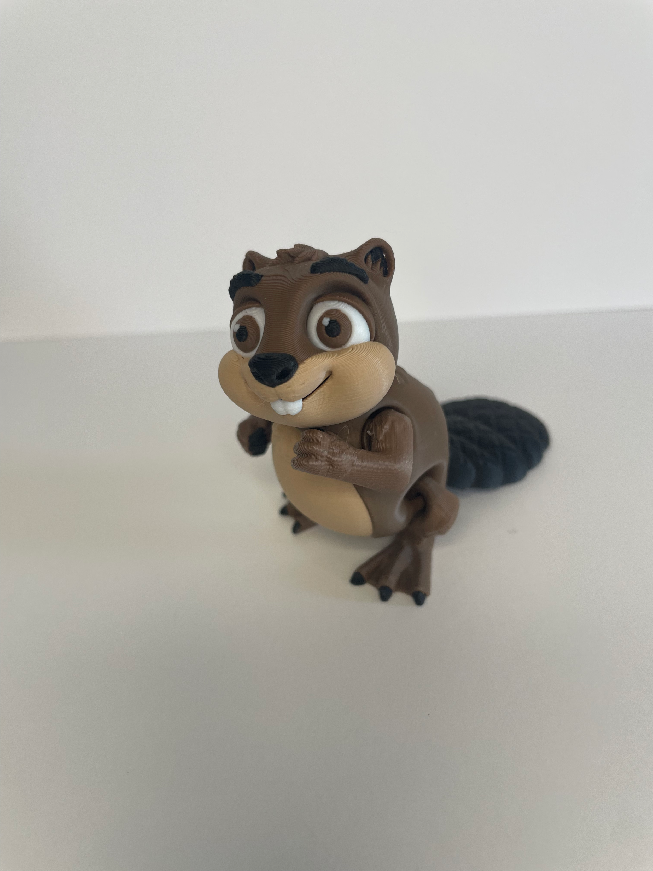 Toy clay figure of a cartoon beaver with large eyes, smiling, with a black tail, on a white surface and background.