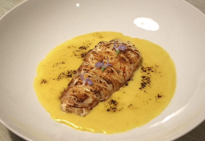 Seared fish fillet topped with microgreens on a bed of yellow sauce in a white bowl.