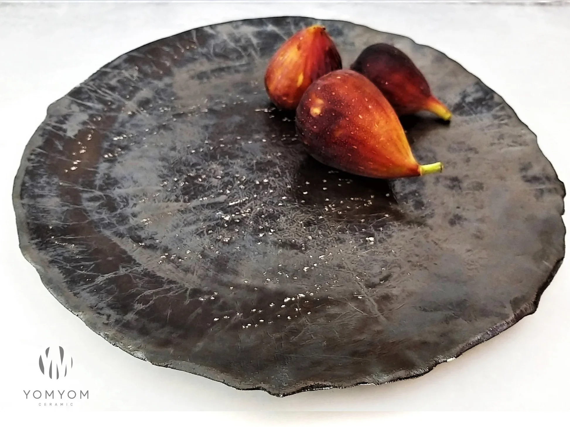 A black ceramic plate with a textured surface, holding three small reddish-brown figs.