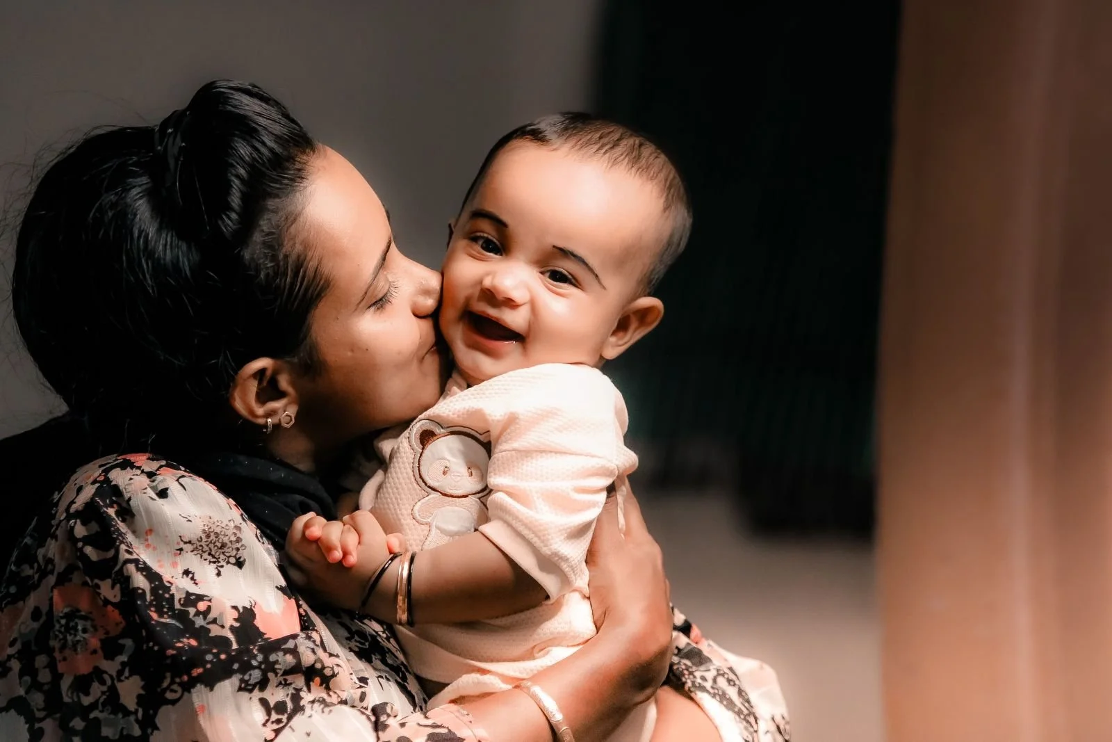 Mother kissing her smiling baby — the kind of bonding that comes with holistic breastfeeding support through Neuroprotective Developmental Care in Singapore