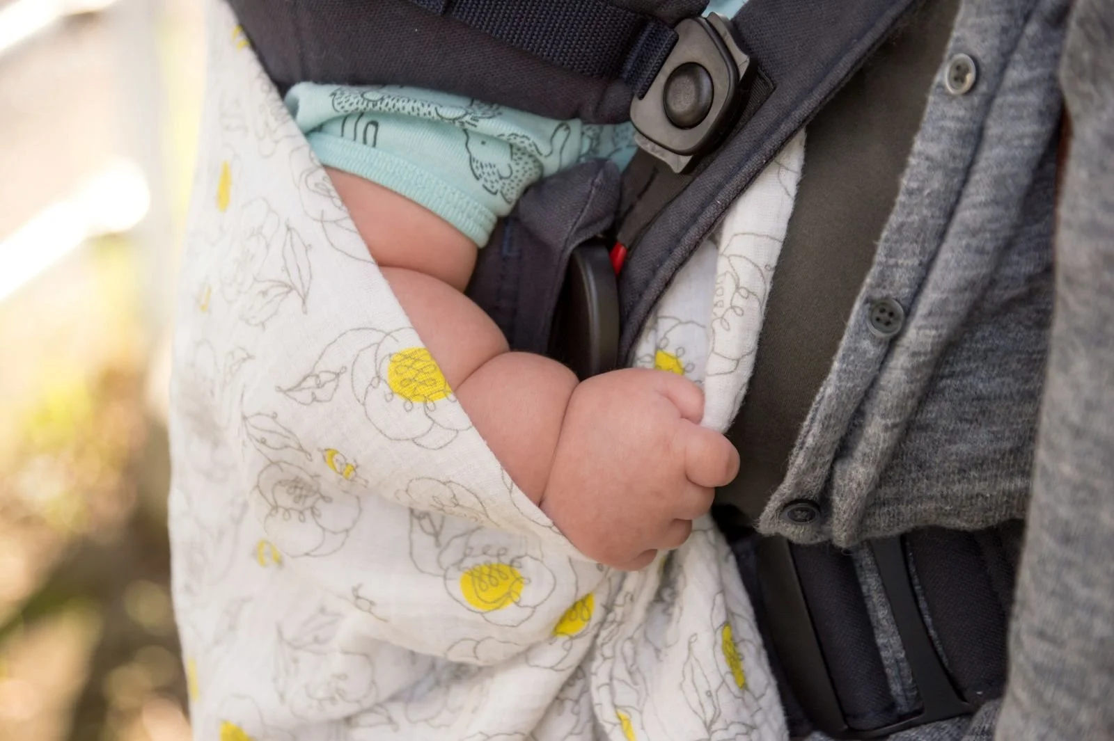 Baby hand relaxing on soft grey carrier sling with mother
