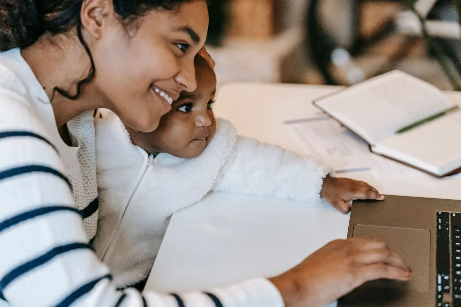 Working mother holding baby while using laptop — balancing breastfeeding and work in Singapore