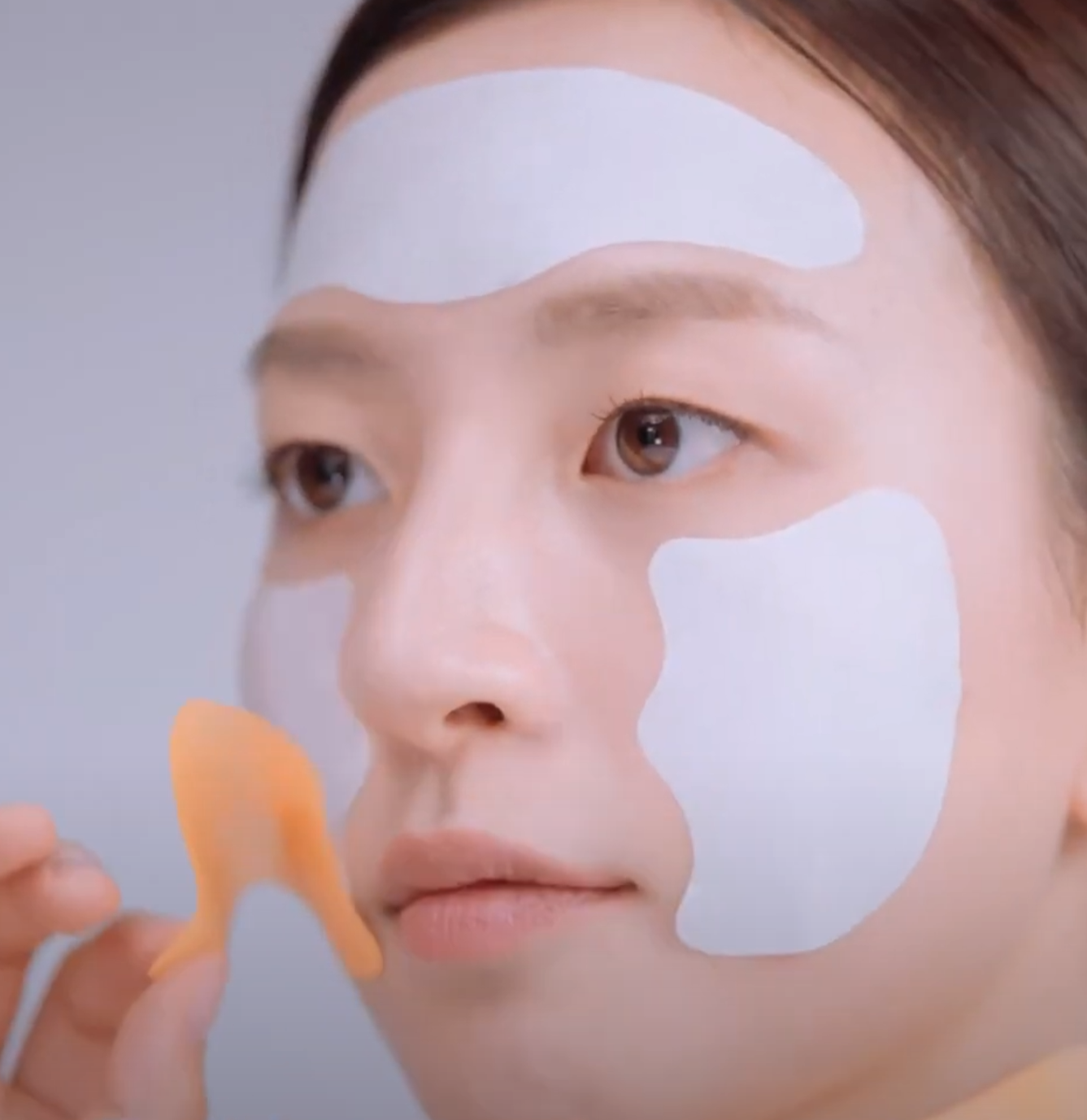 Woman with white face patches applying skincare with a spatula.