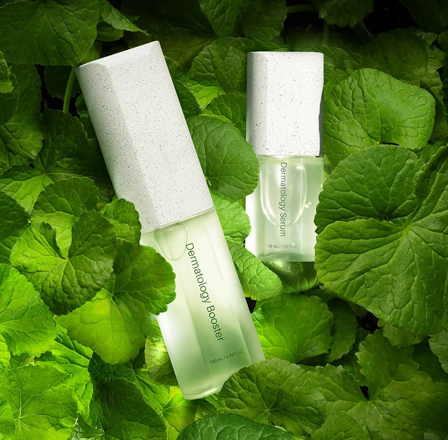 Two bottles of skincare serum labeled 'Dermatology Booster' and 'Dermatology Serum' surrounded by green leaves.