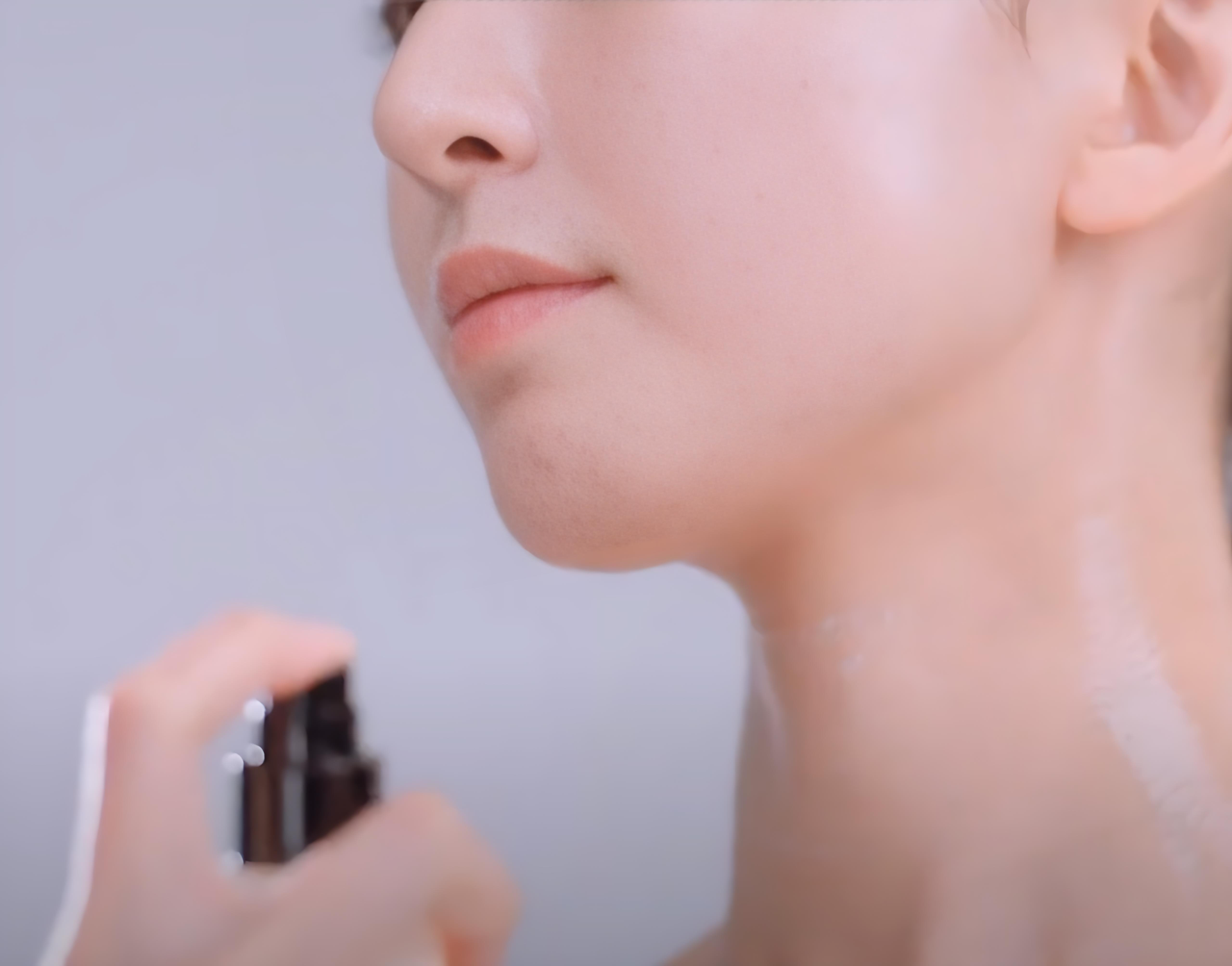 Close-up of a woman applying perfume to her neck.