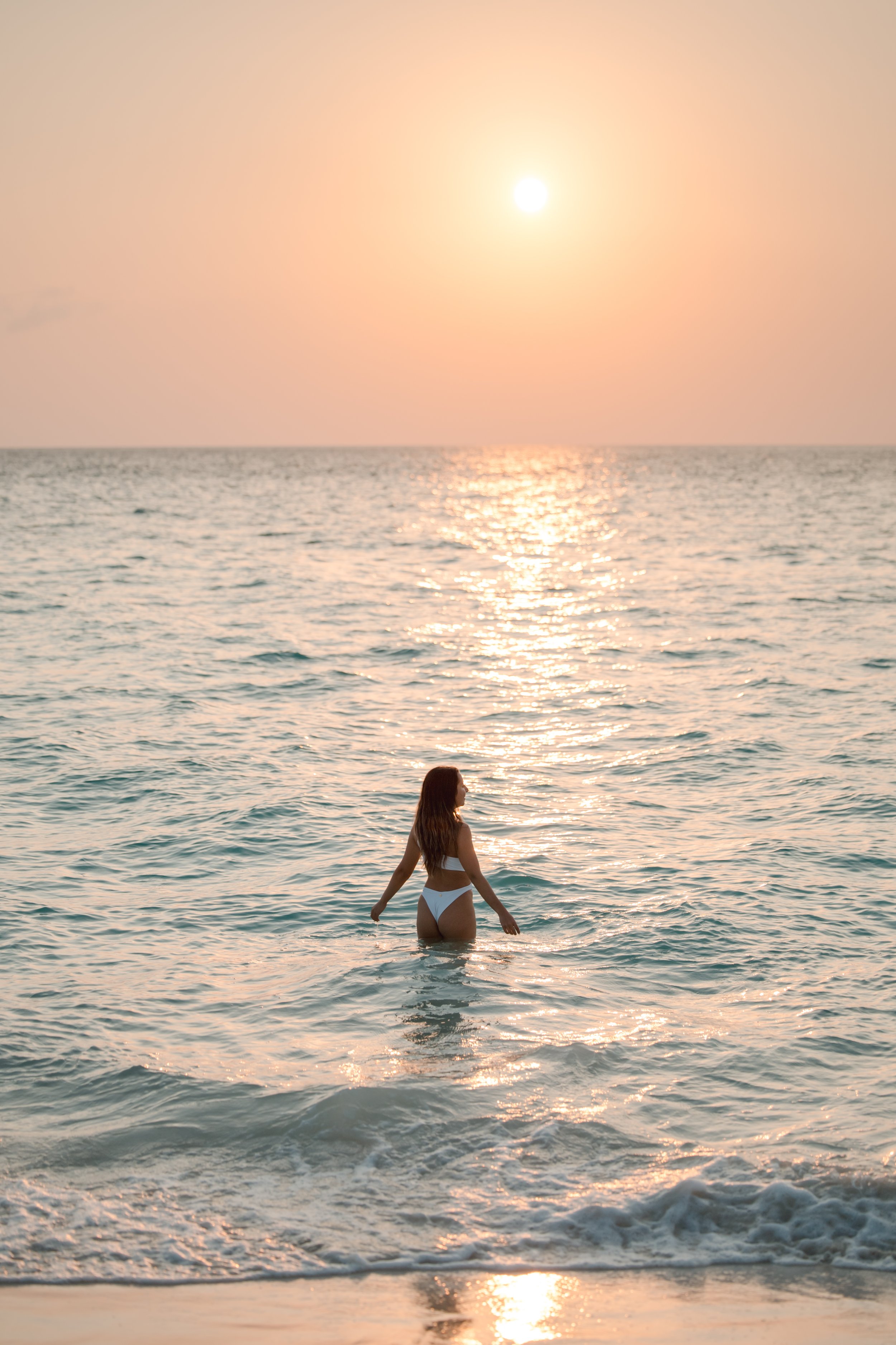 Woman standing in ocean at sunset