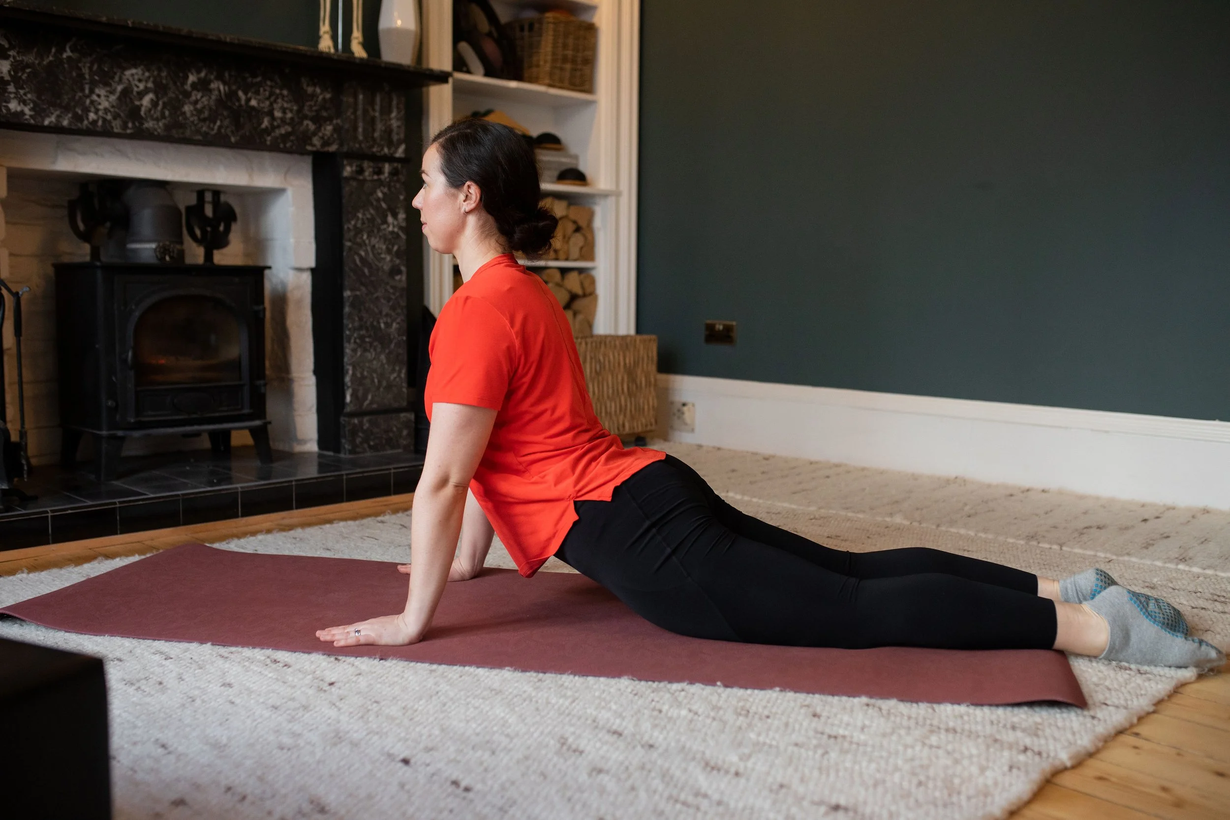 Ailsa lying face down on a mat, lifting her chest away from the floor in a Pilates swan exercise.