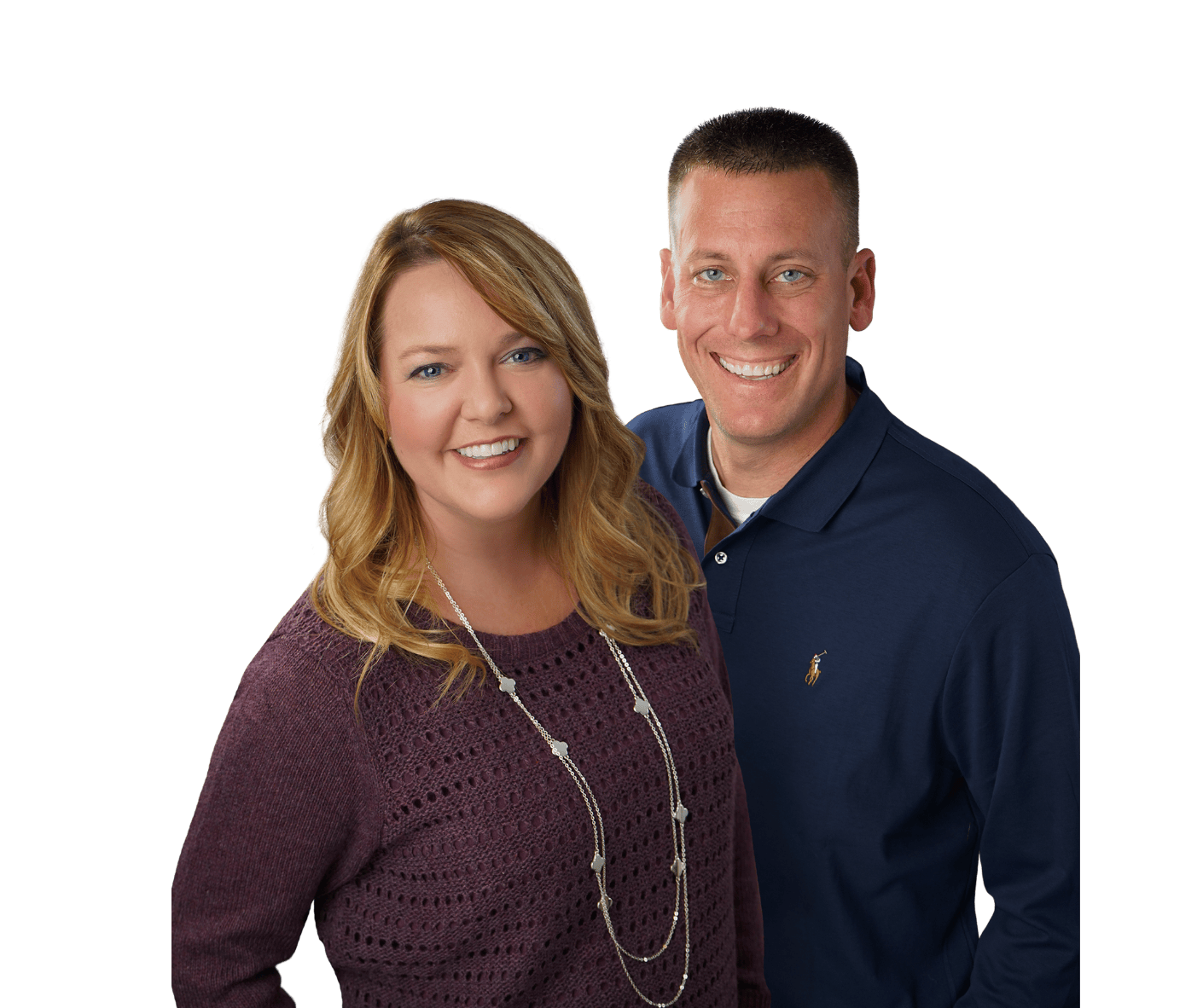 A smiling woman with red hair wearing a purple knitted sweater and a long necklace standing next to a smiling man with short hair wearing a navy blue polo shirt.