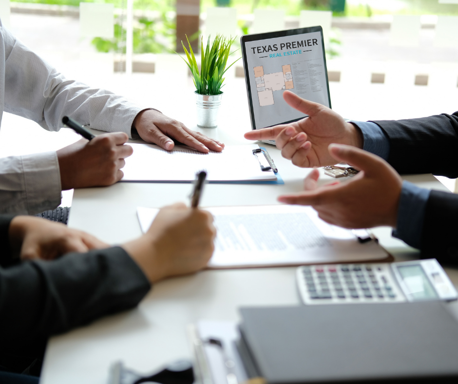 Business meeting with two people discussing real estate plans, one showing a tablet labeled 'Texas Premier Real Estate' with a floor plan, on a white table with documents, a calculator, and a plant in the background.