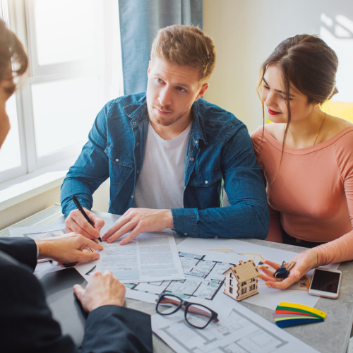 Man and woman sitting at a table with a real estate agent, discussing documents and prospective house details