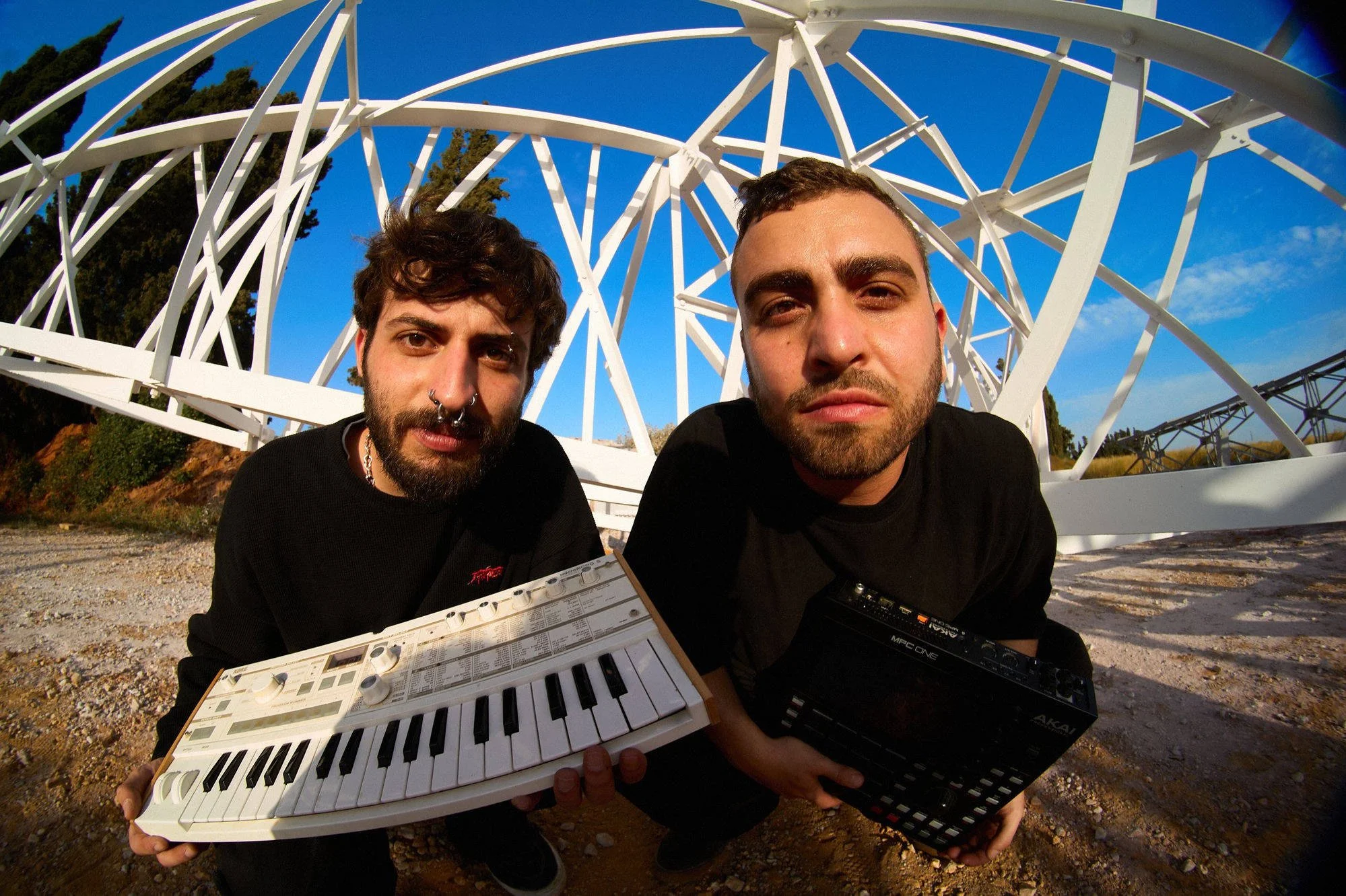 Cybersloth electronic music duo holding synthesizers in front of a steel crane structure.