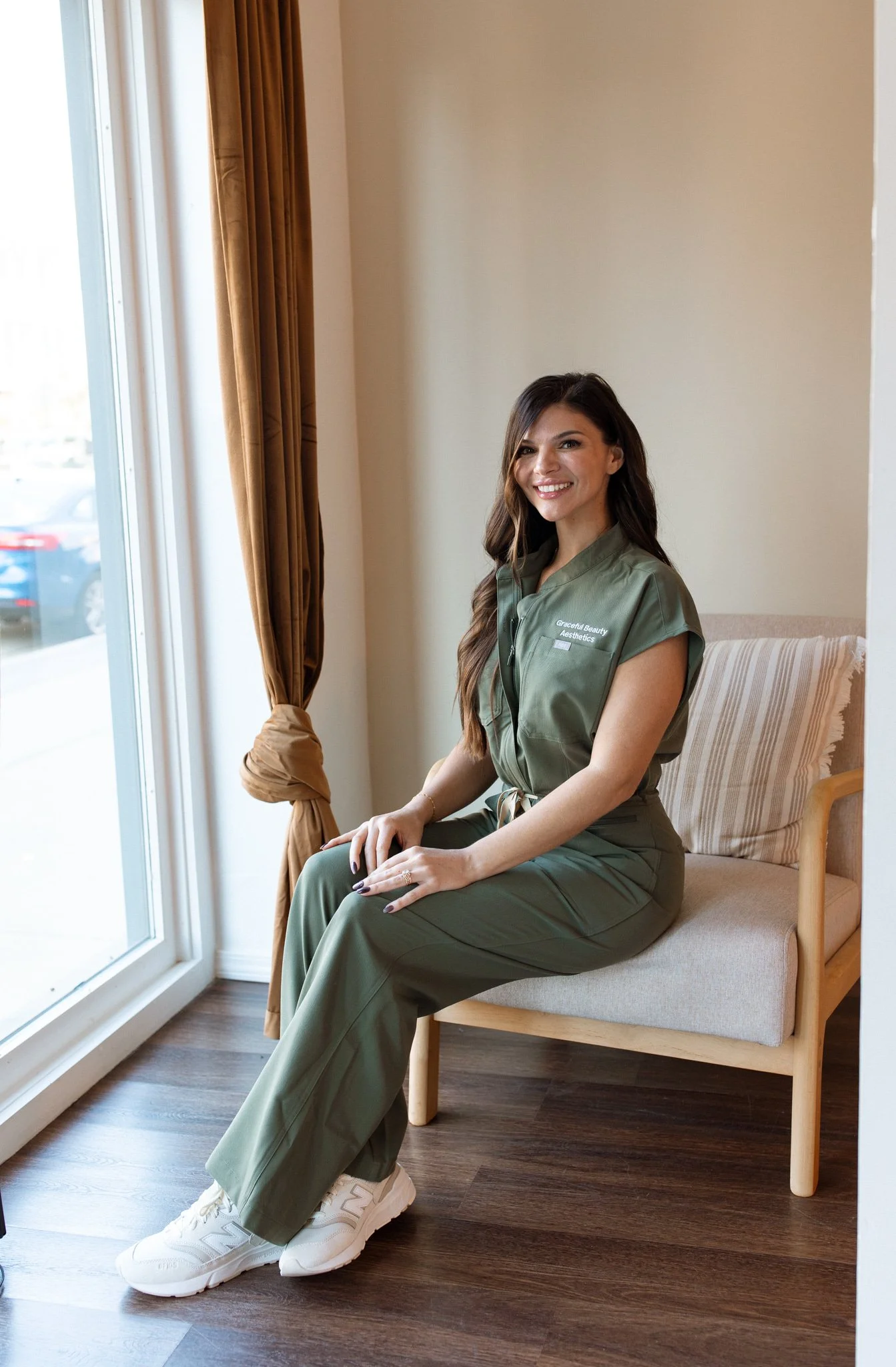 Smiling woman with long wavy hair wearing a black shirt standing against a plain background.