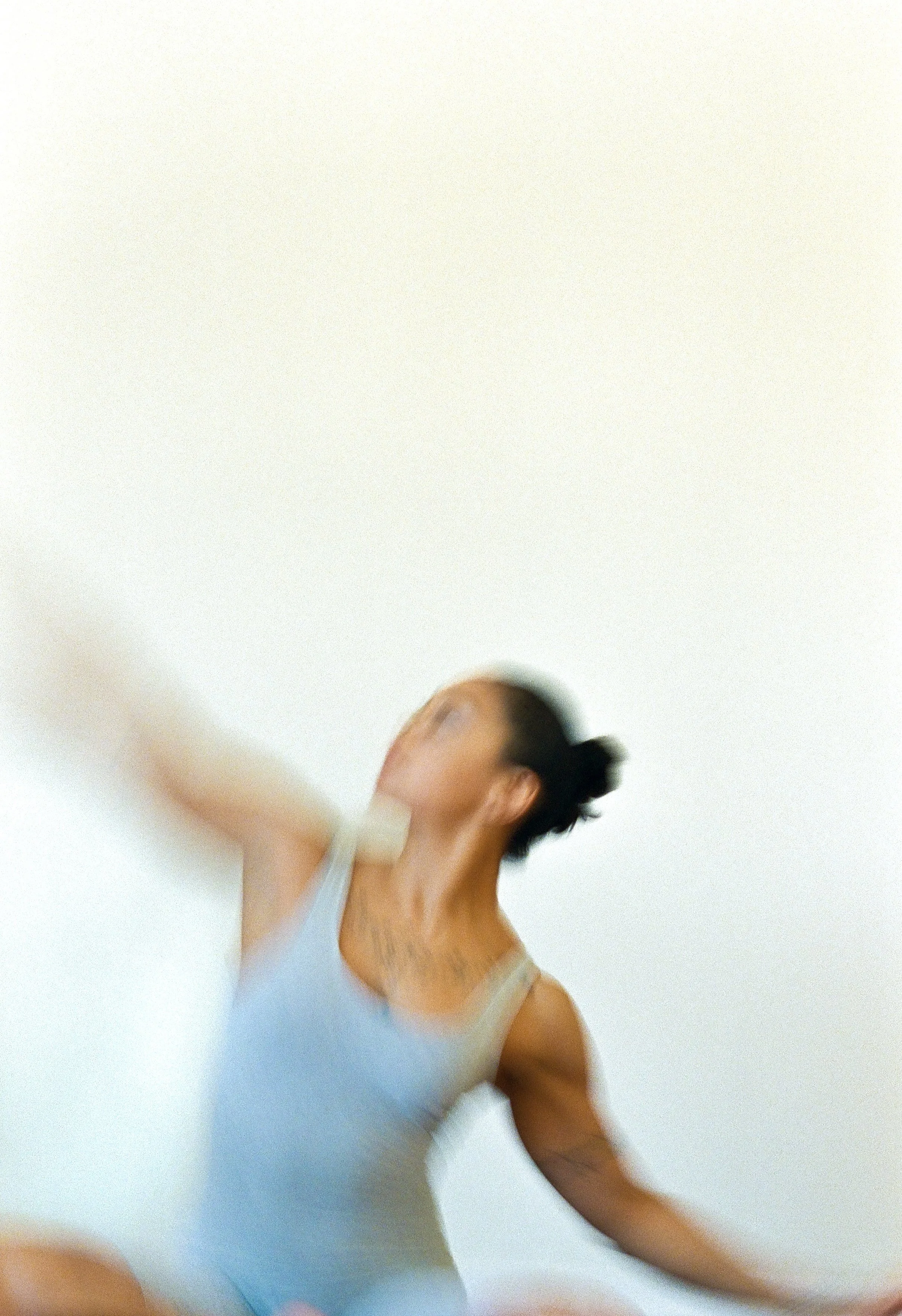 A woman in a light blue tank top is practicing dance or yoga against a plain white background.