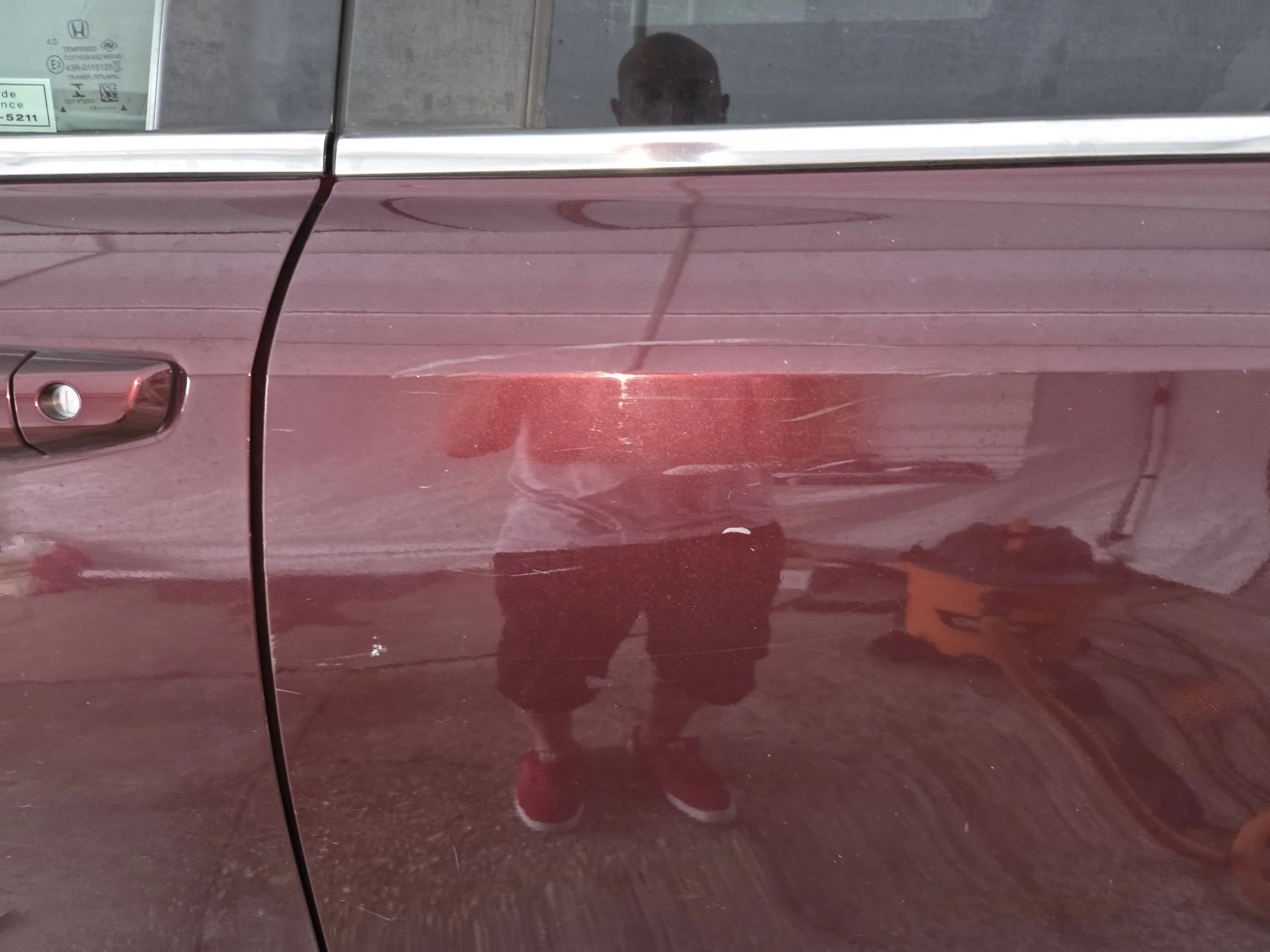 Close-up of a maroon car door reflecting the person taking the photo after buffing.