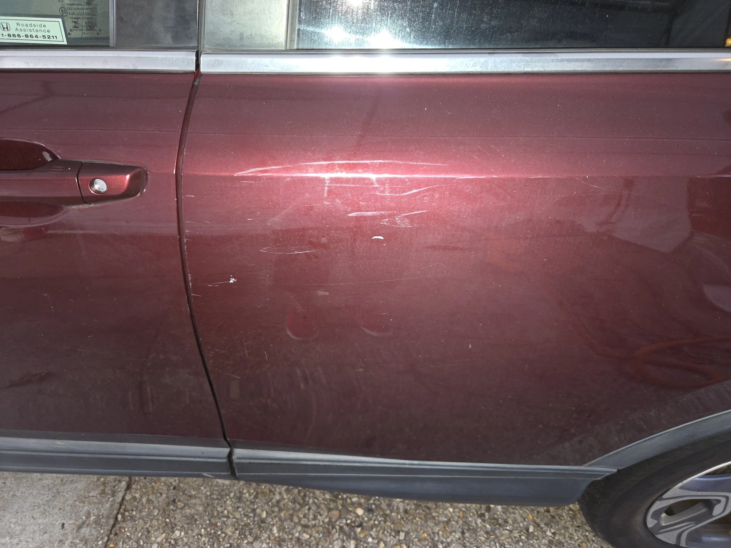 Close-up of a maroon car door with visible scratches and dents.