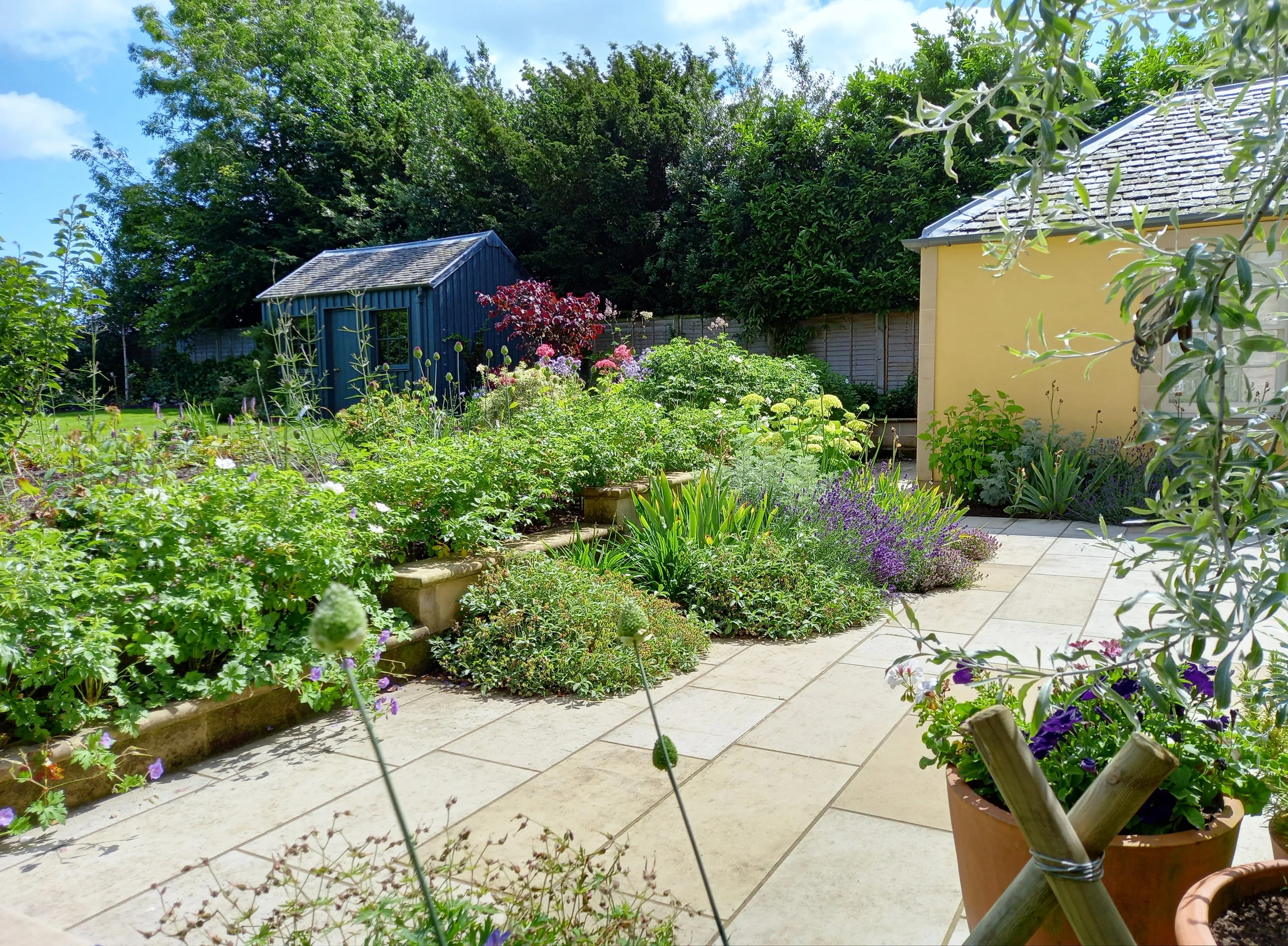 Country garden with a cream terrace with lush planting beds.