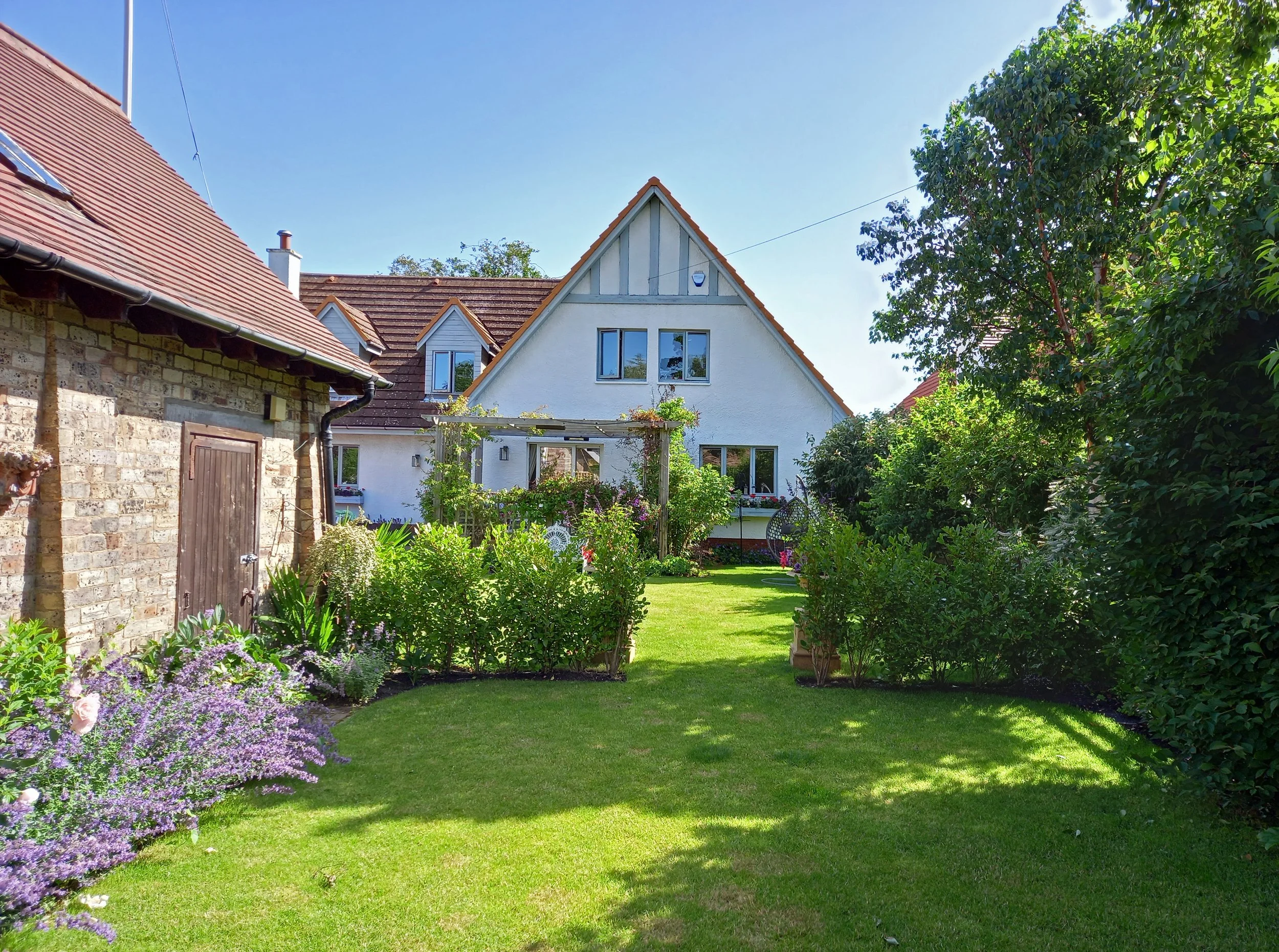 A white house with a long garden stretching away from it with green hedging and flowers along the borders.