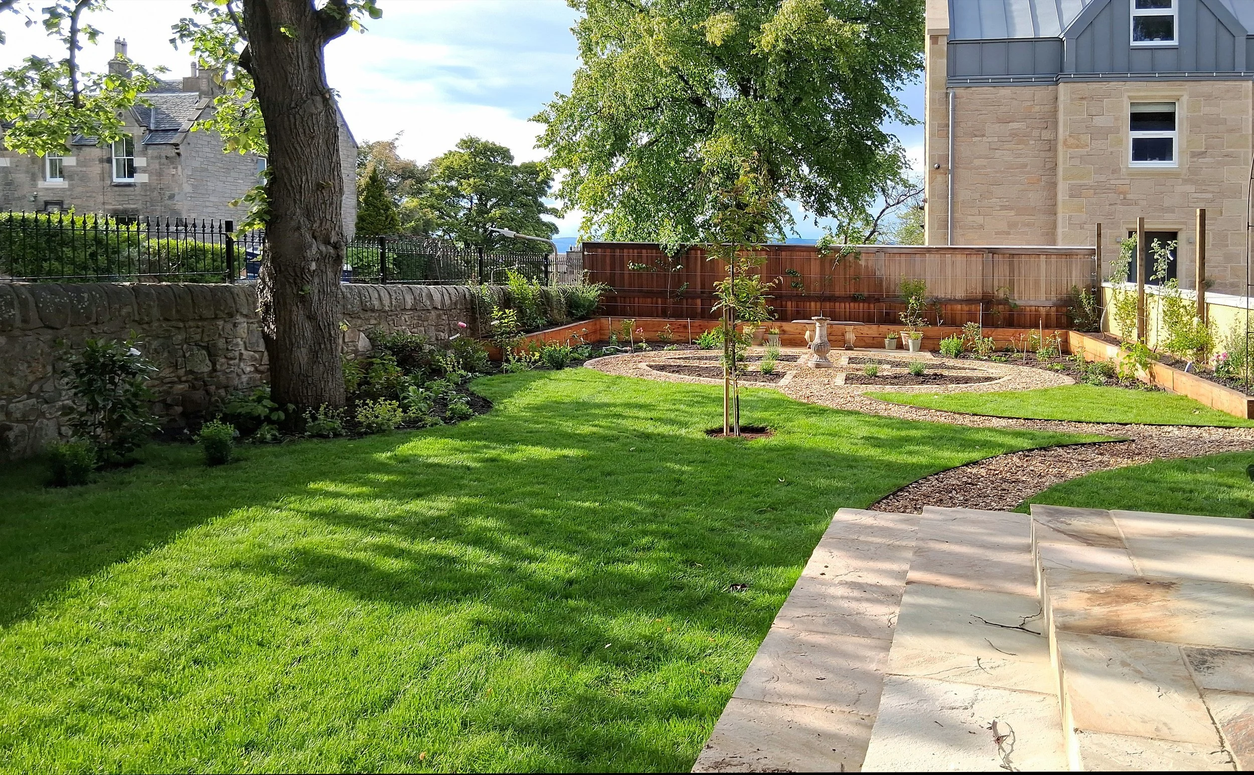 Newly designed garden with a Potager at one end and a focal tree. Cream terrace with extra wide steps leading down to the grass.