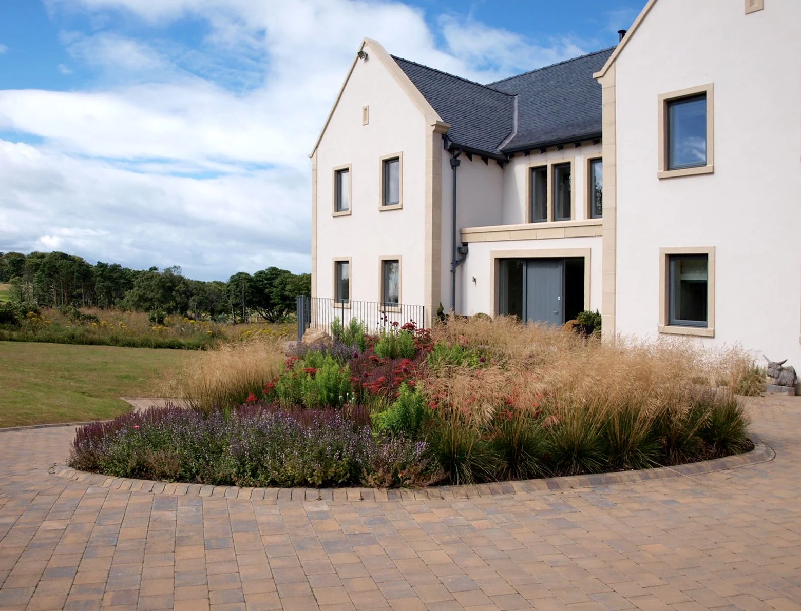 Grasses and flowering perennials in front of a large house.