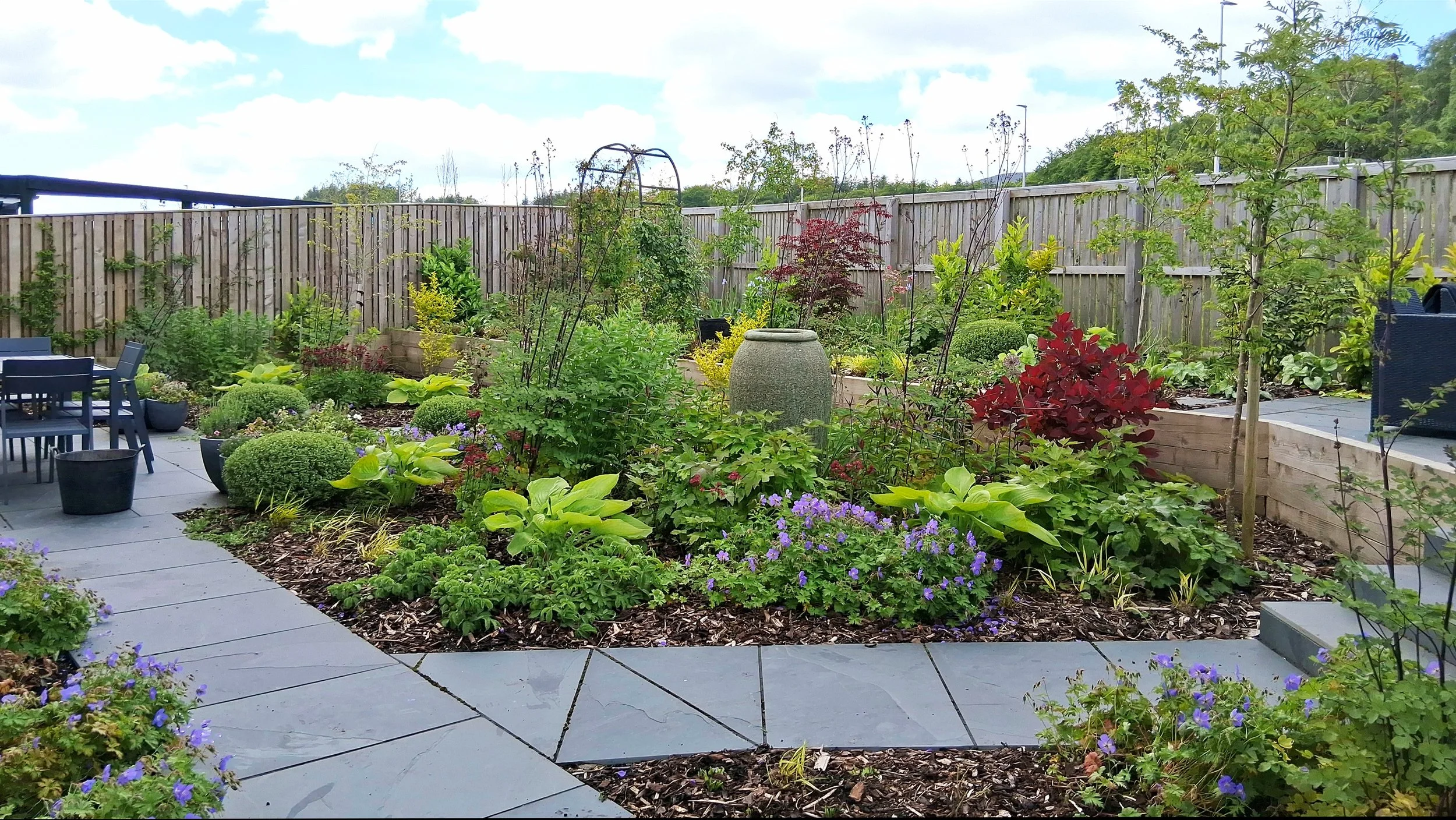 A colourfully planted garden with slate coloured paths and lots of different foliage colours.