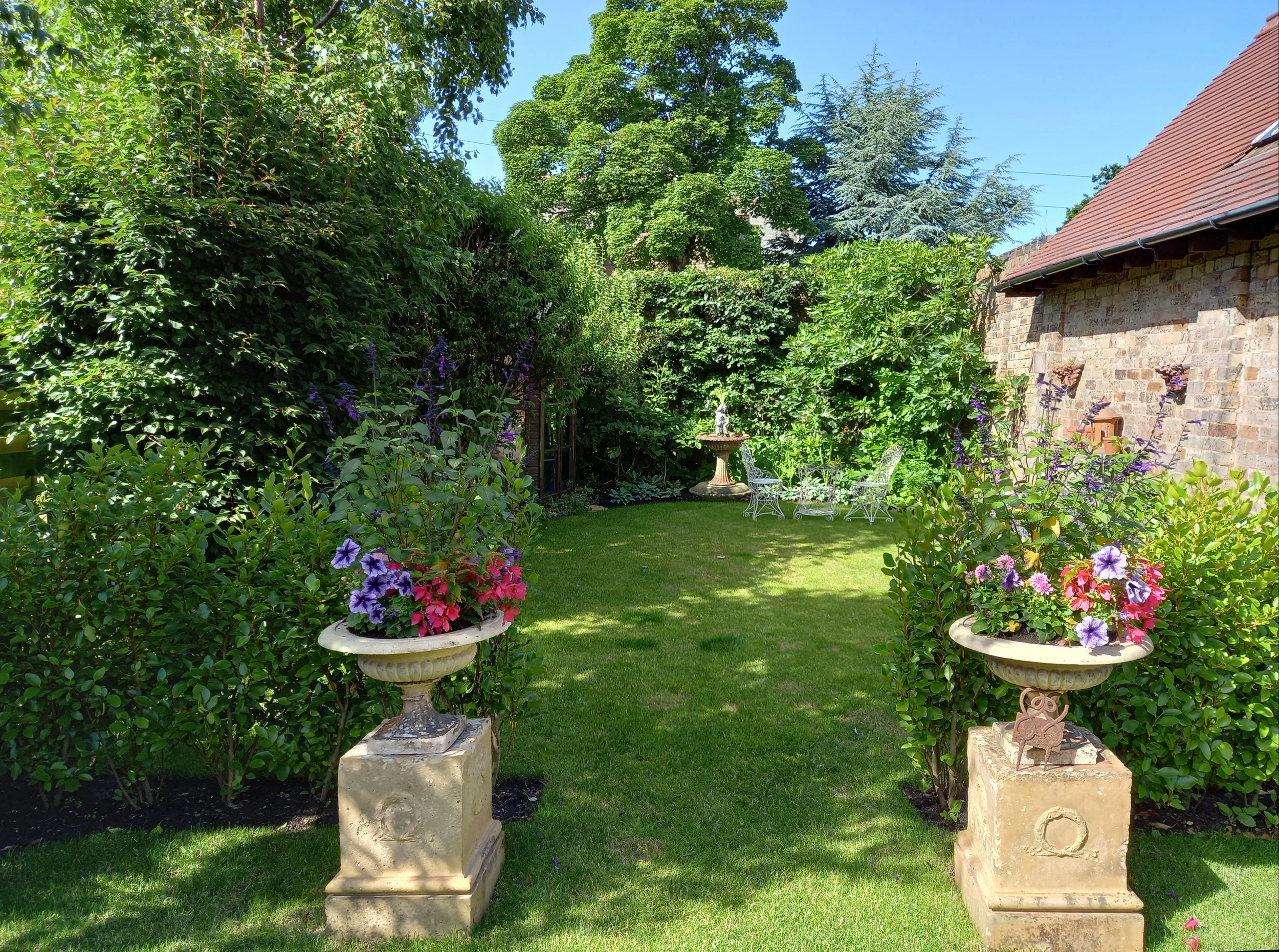 Two identical urns frame an opening into a new part of a garden with a focal point at the bottom. The urns a full of seasonal colour.