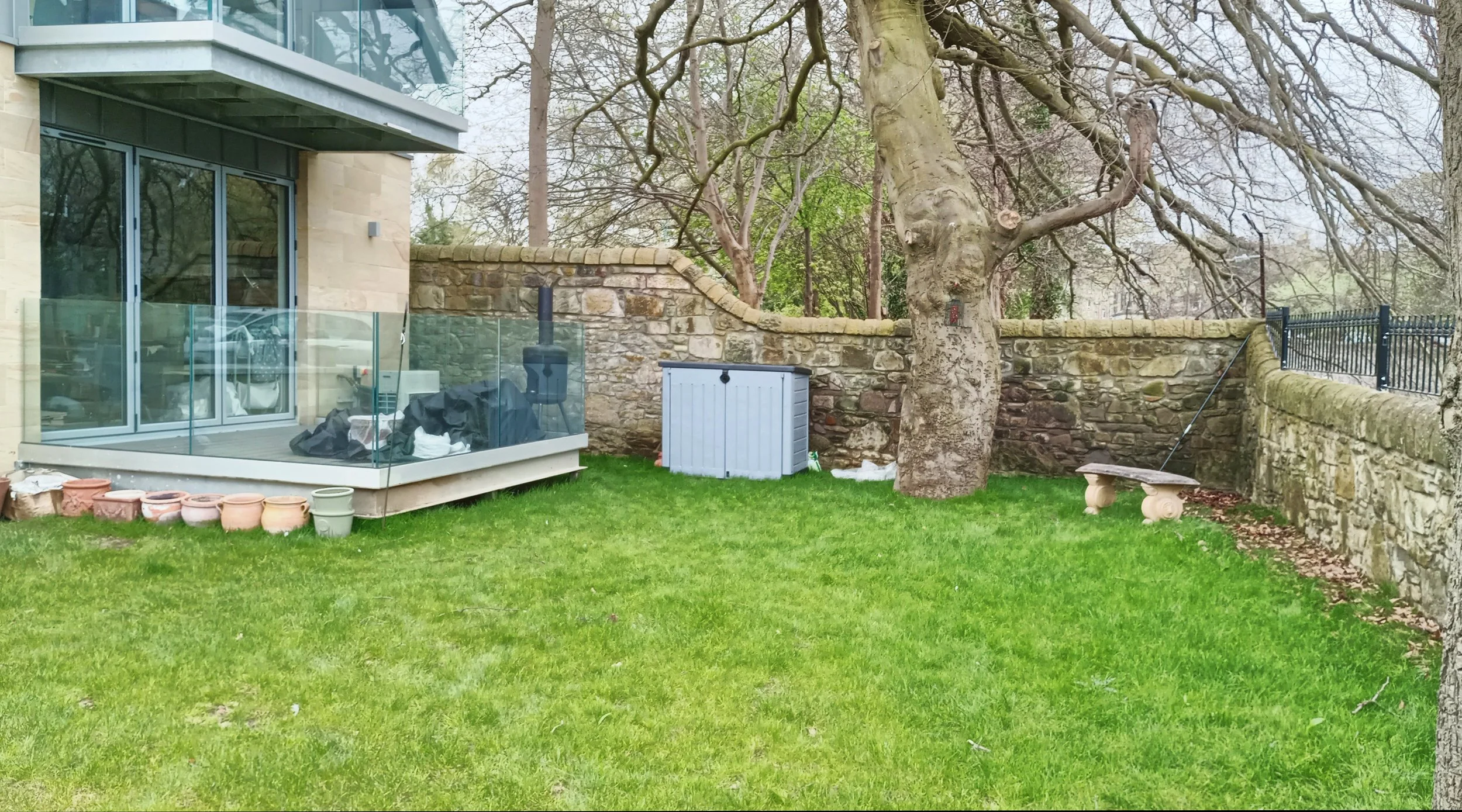New build garden with an enclosed terrace with glass fencing around it. 