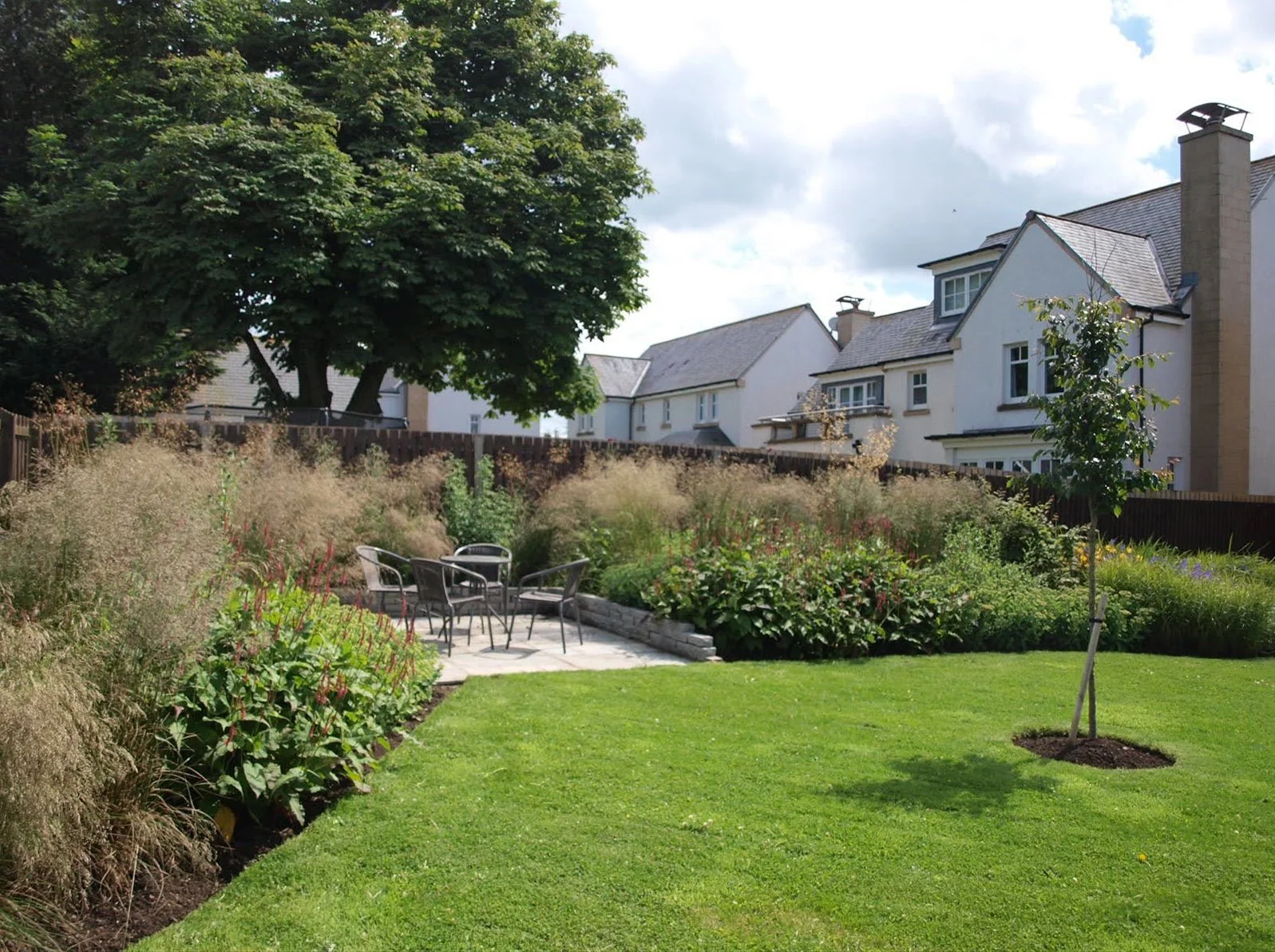 Deep naturalistic planting surrounding a patio with table and chairs.