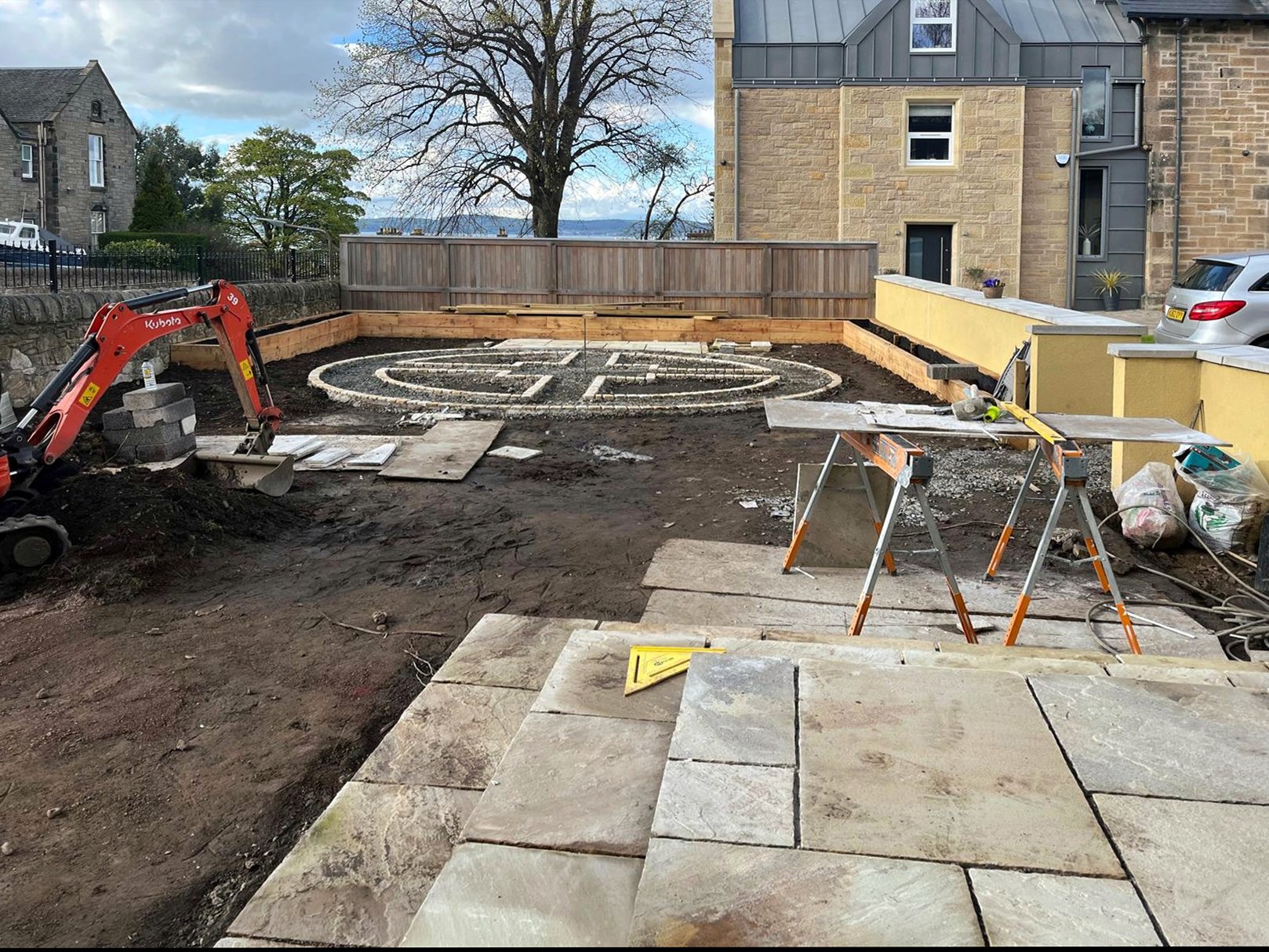 A garden design being constructed. Bare soil and building materials and tools are scattered around.