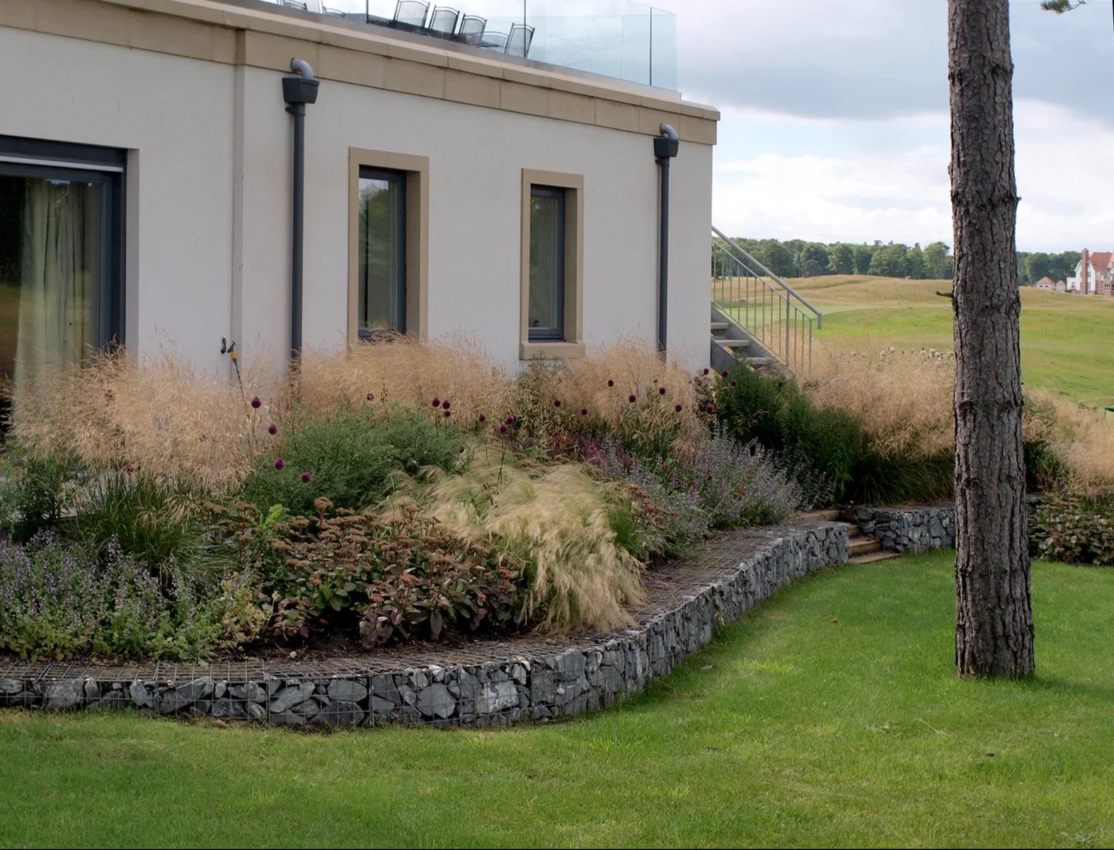 Grasses and ornamental perennials in a raised bed adjacent to a house.