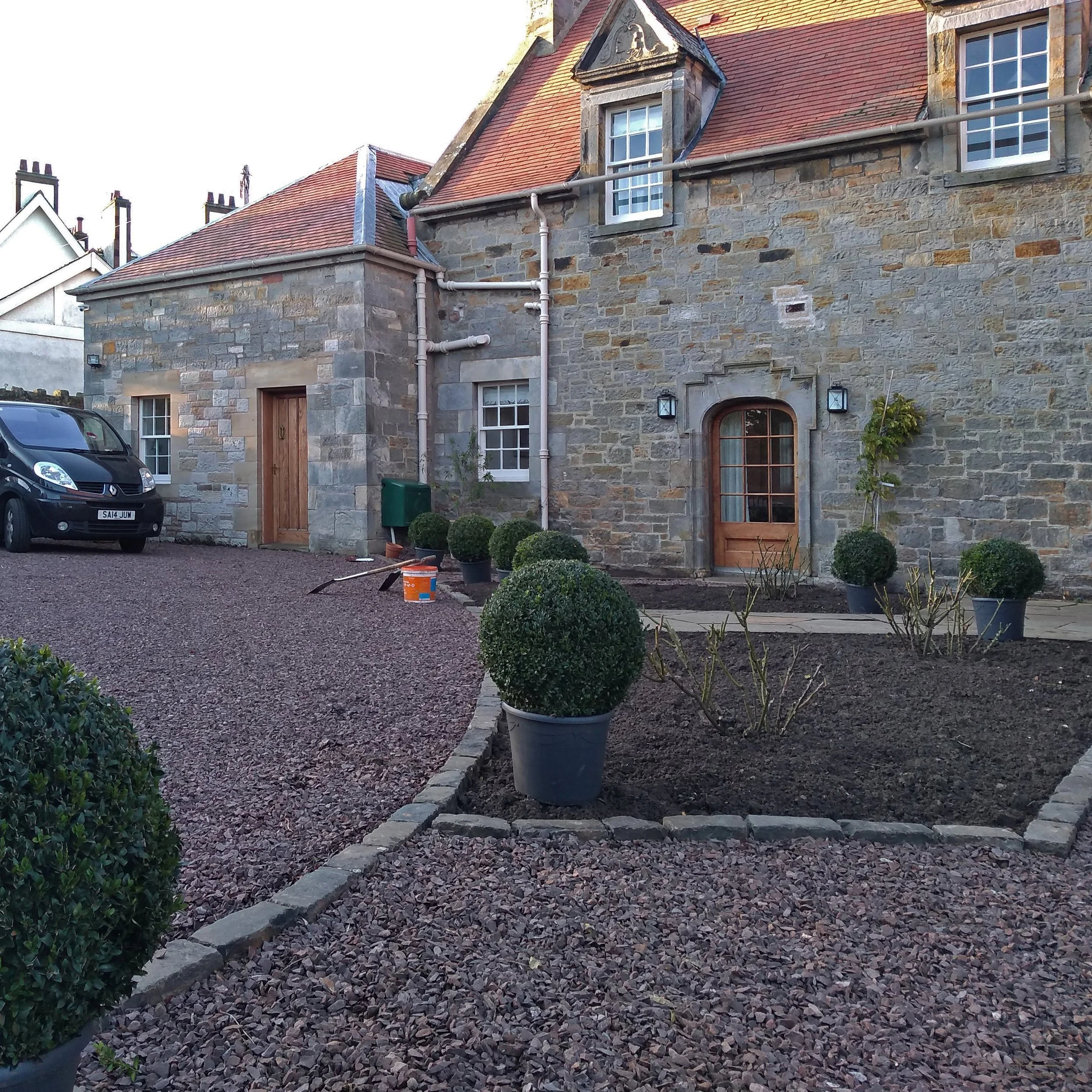 Bare curved planting beds in front of a historic house.