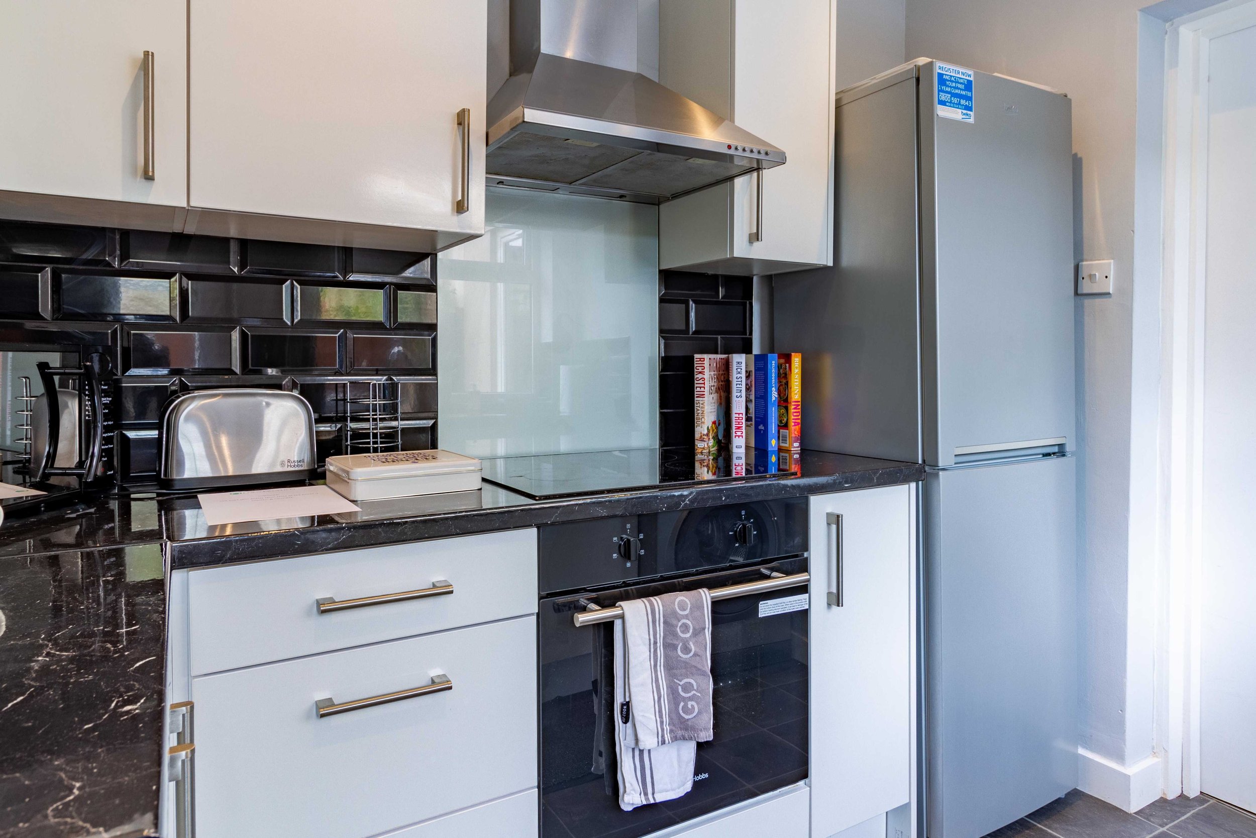 Modern kitchen with stainless steel appliances, black tile backsplash, toaster, oven, and refrigerator.