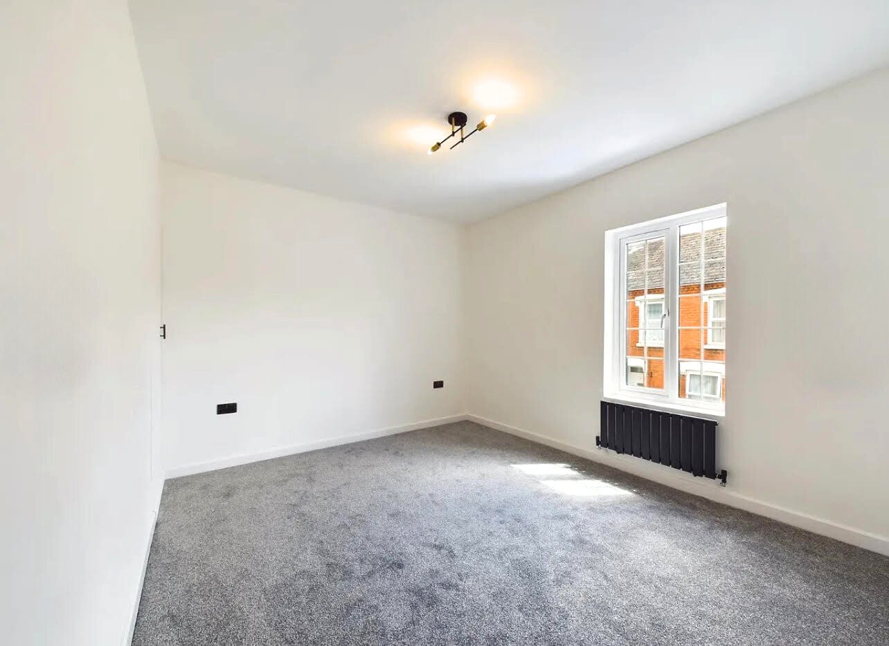 Empty room with gray carpet, white walls, a ceiling light fixture, window with view, and black radiator.