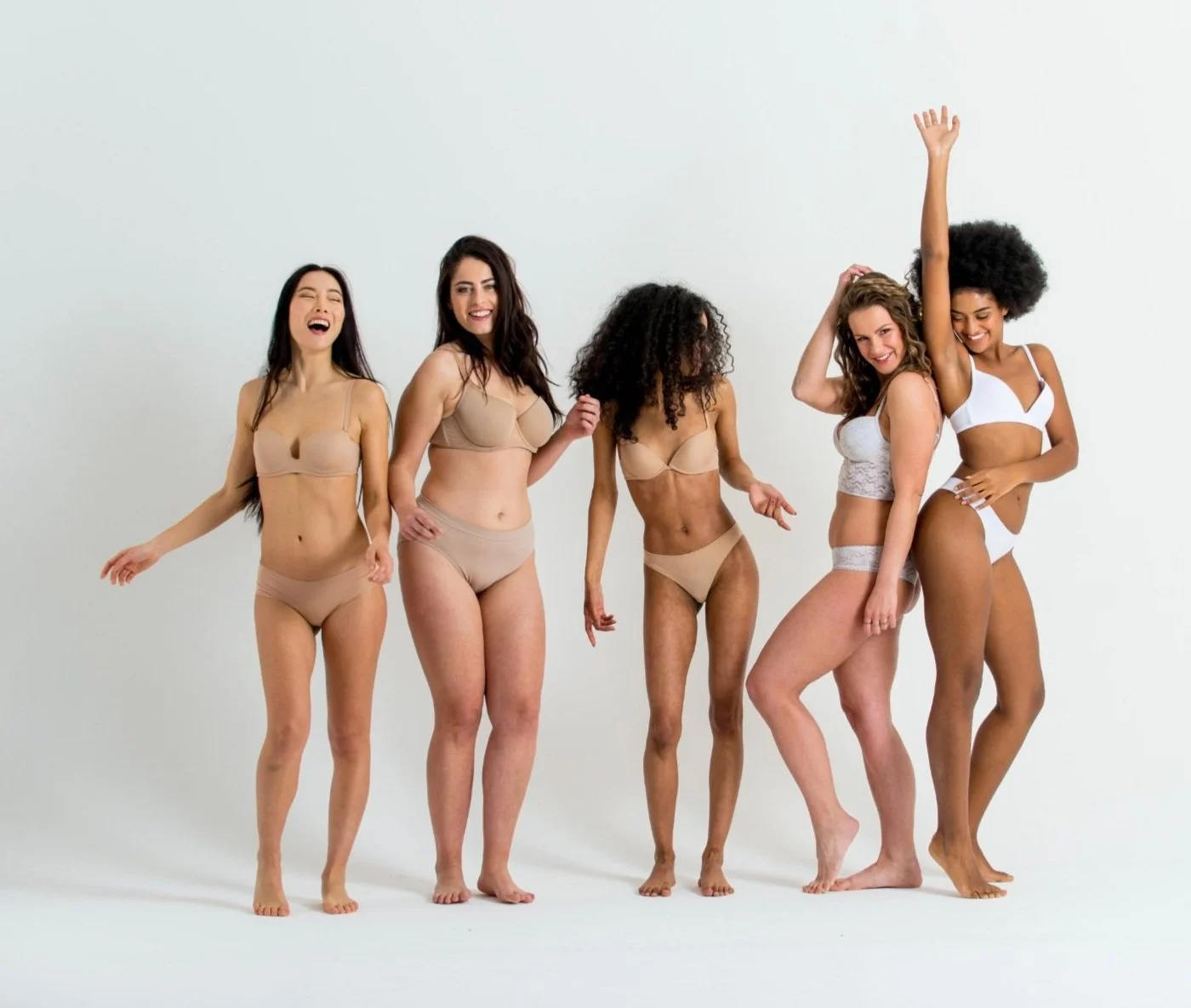 Six women of diverse ethnicities in underwear, standing together and smiling against a plain white background.