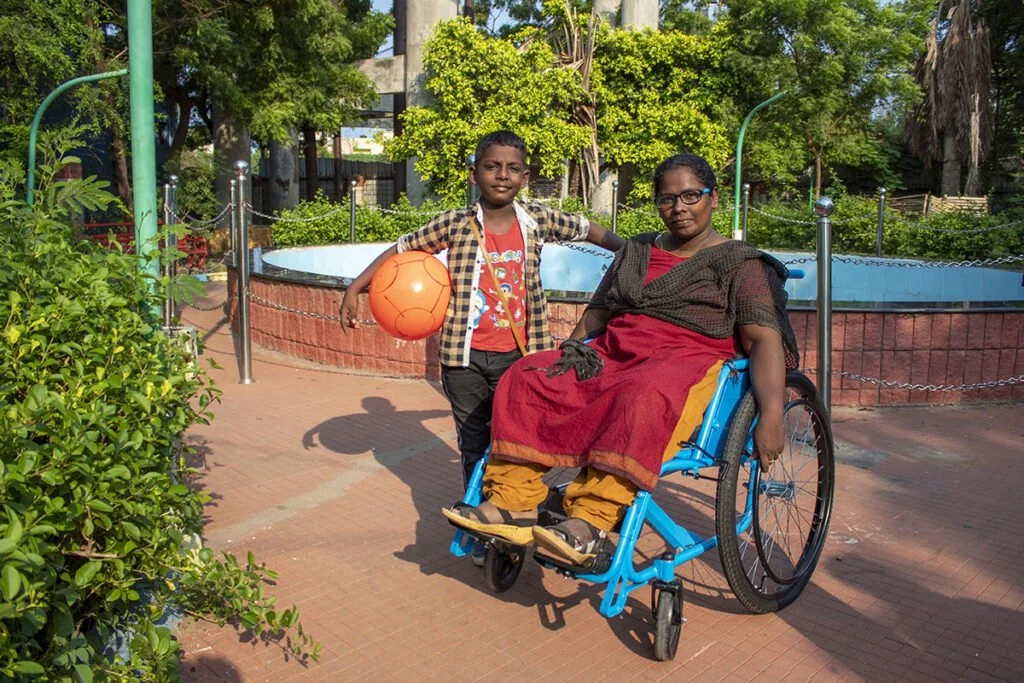 Group of people in wetsuits on a rocky beach with a rainbow in the sky, blue skies, and ocean in the background.