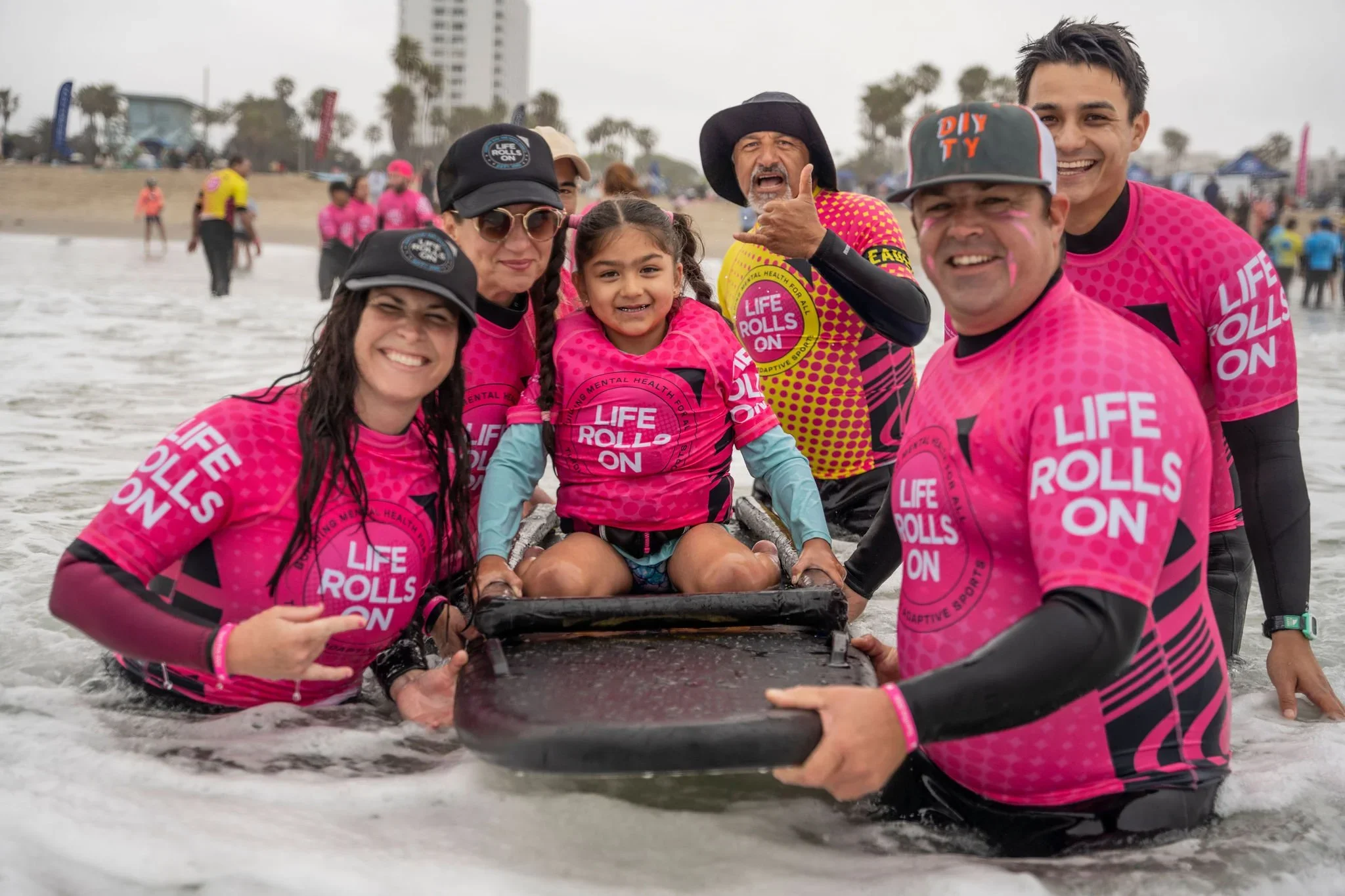 Woman in wetsuit standing with a surfboard at the beach, looking out at the ocean during sunset.