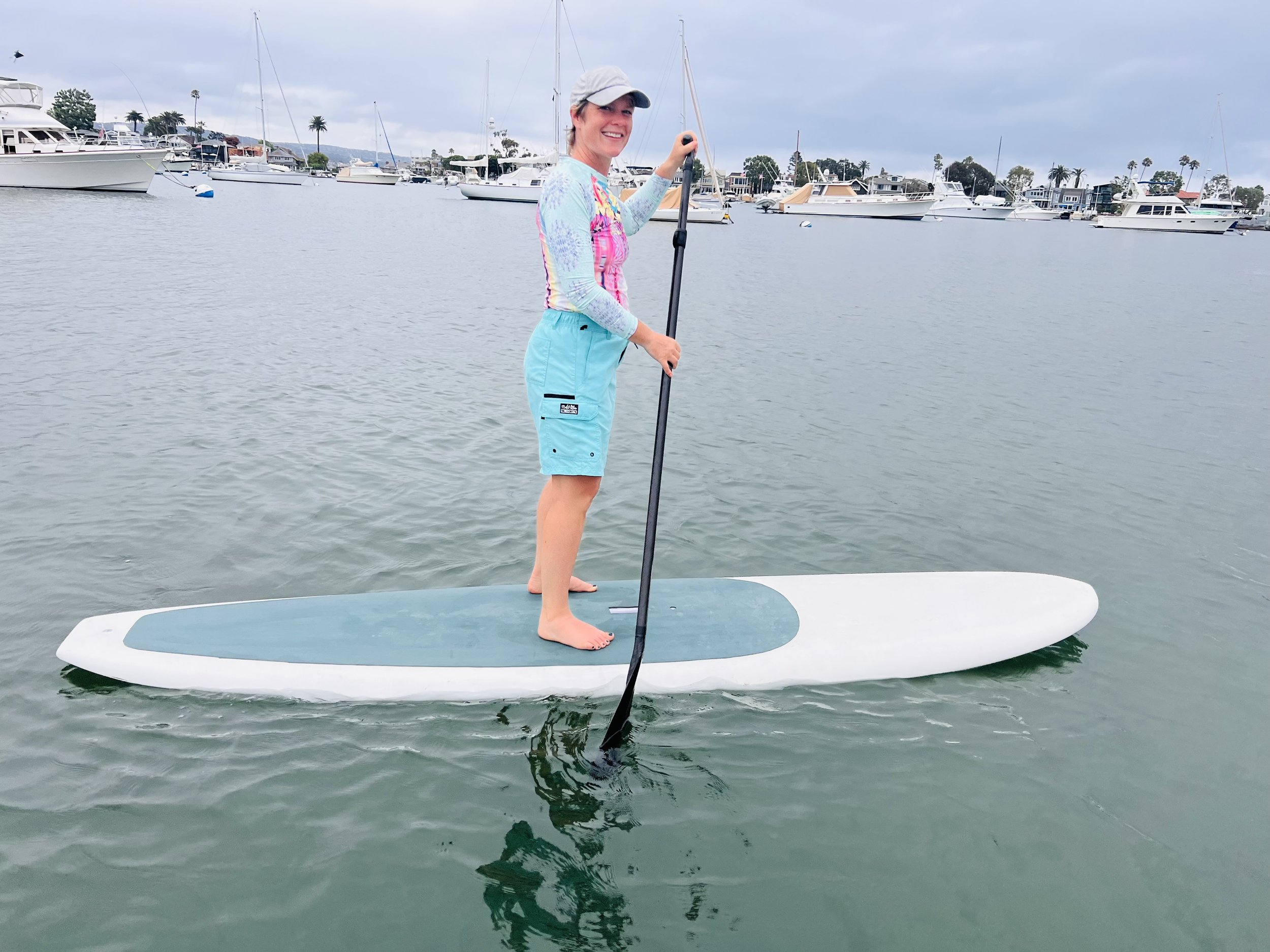 Person paddleboarding on calm water with boats in background.