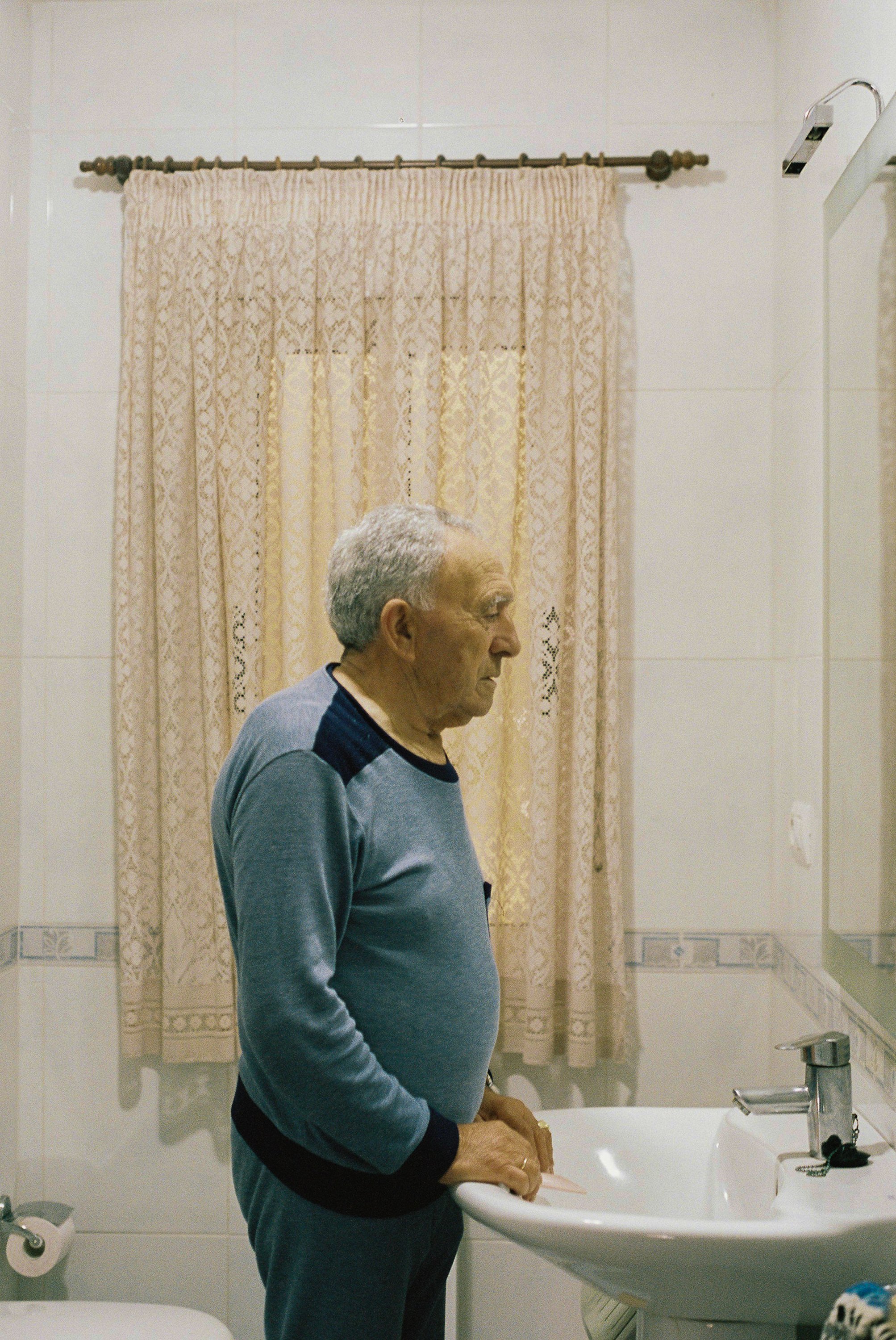 Elderly man looking at himself in the mirror in the toilet.