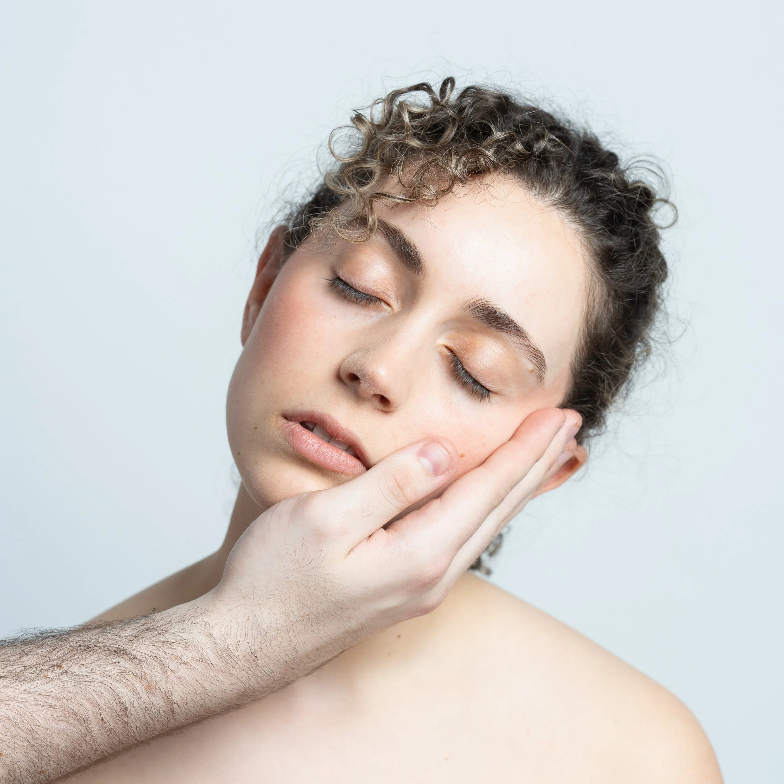 Portrait in the studio of a girl's face being held by someone's hand.
