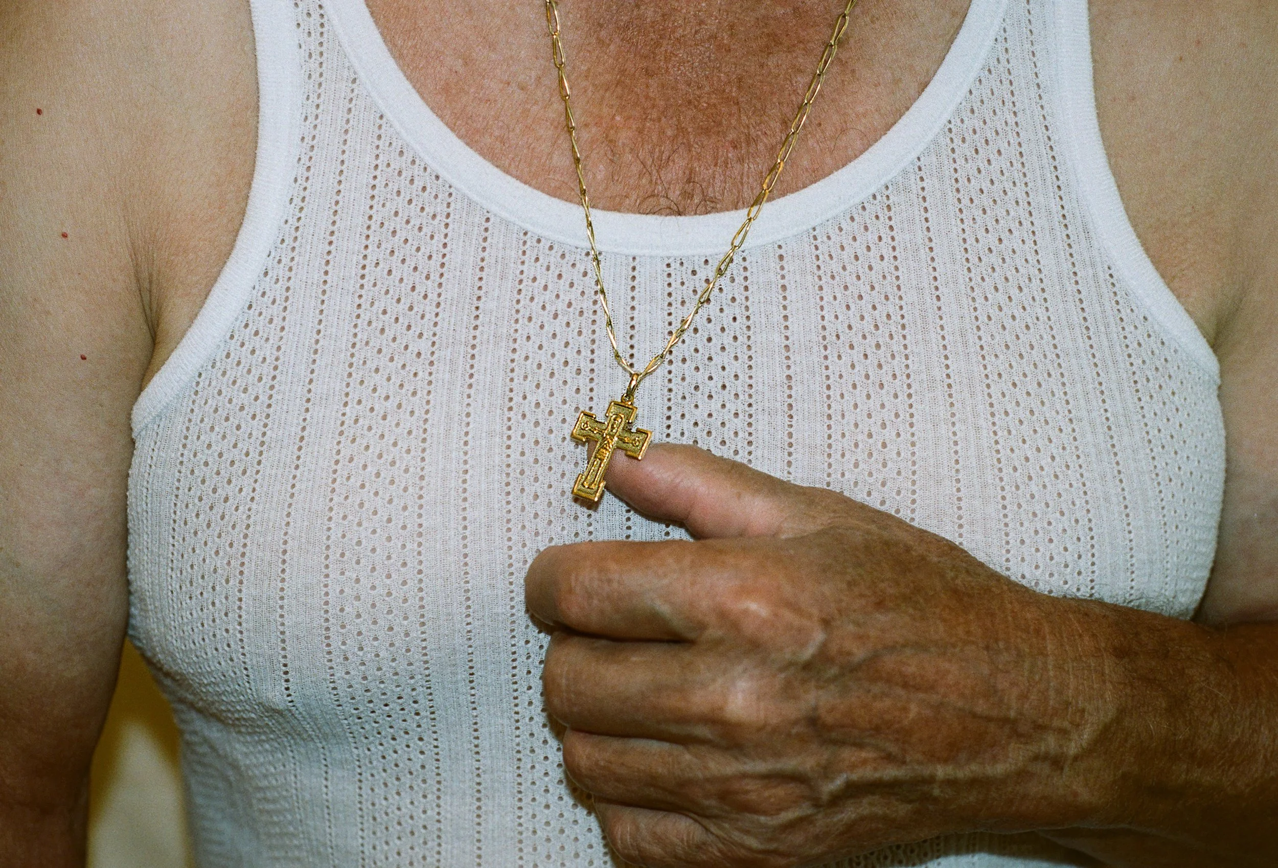 Shot of elderly man's chest holding cross chain with hand.