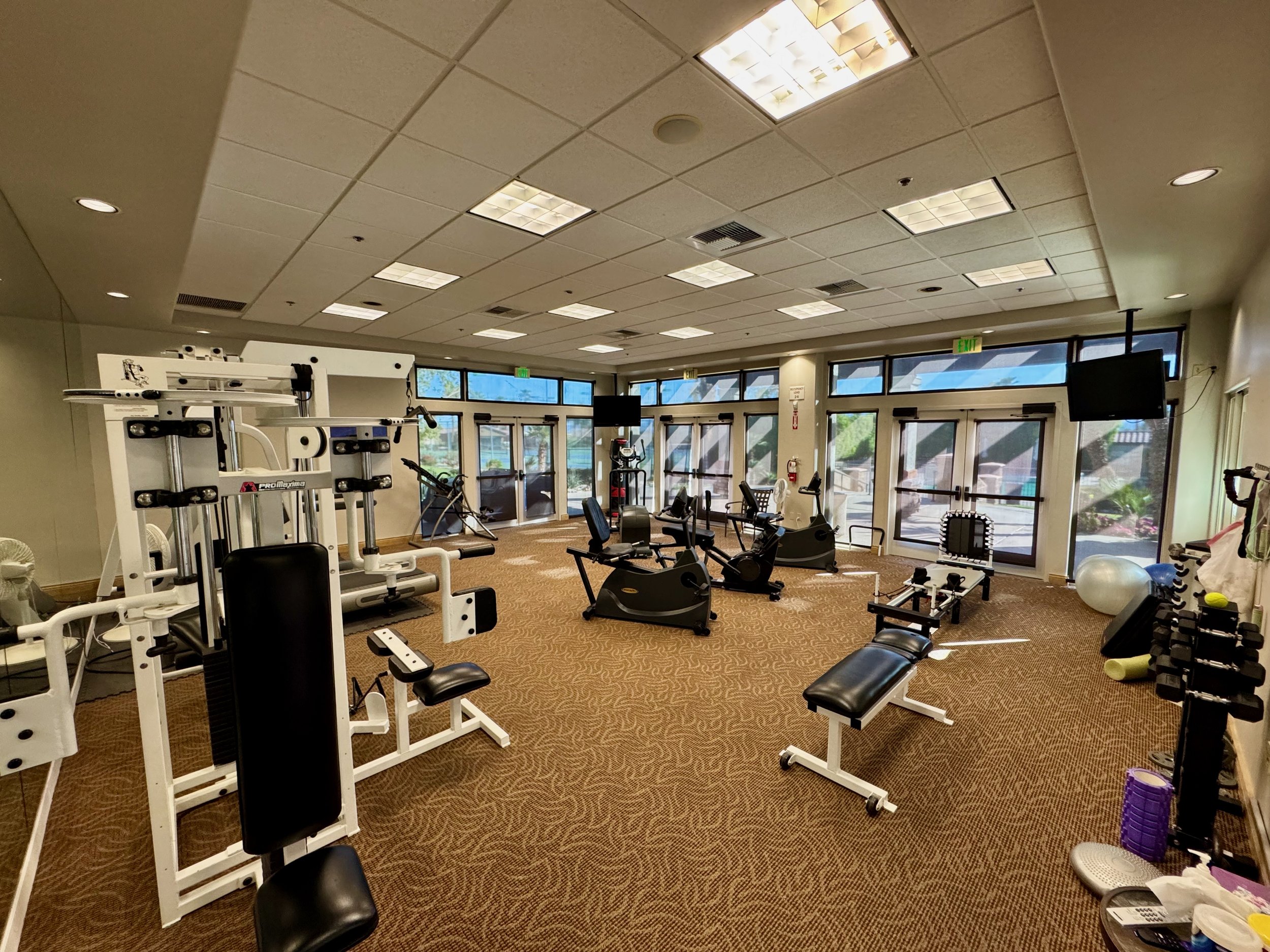 Fitness center with various exercise equipment including weight machines, stationary bikes, dumbbells, and benches.