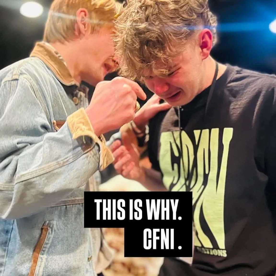 Two young men sharing an emotional moment, tears in their eyes, one wearing a black graphic T-shirt, and the other in a light denim jacket. The scene suggests a heartfelt connection or celebration. Text overlay reading 'This is why. CFNI.'