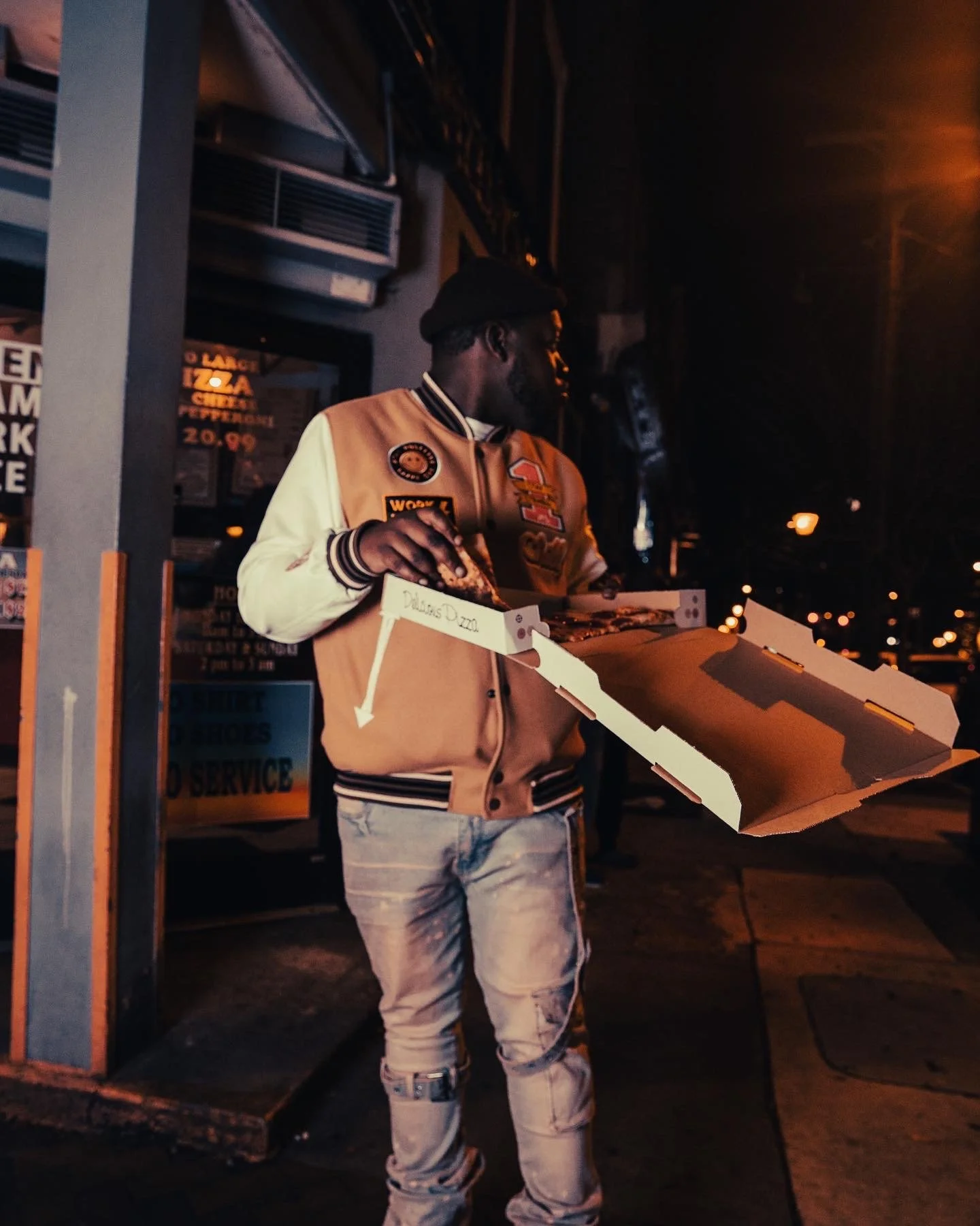 Person holding open pizza box on street at night